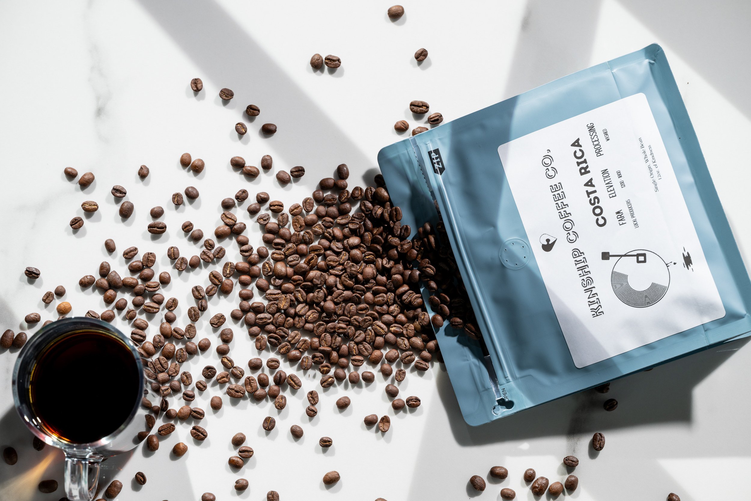 Kinship Coffee Co bag with scattered beans on white marble, specialty coffee brand photography
