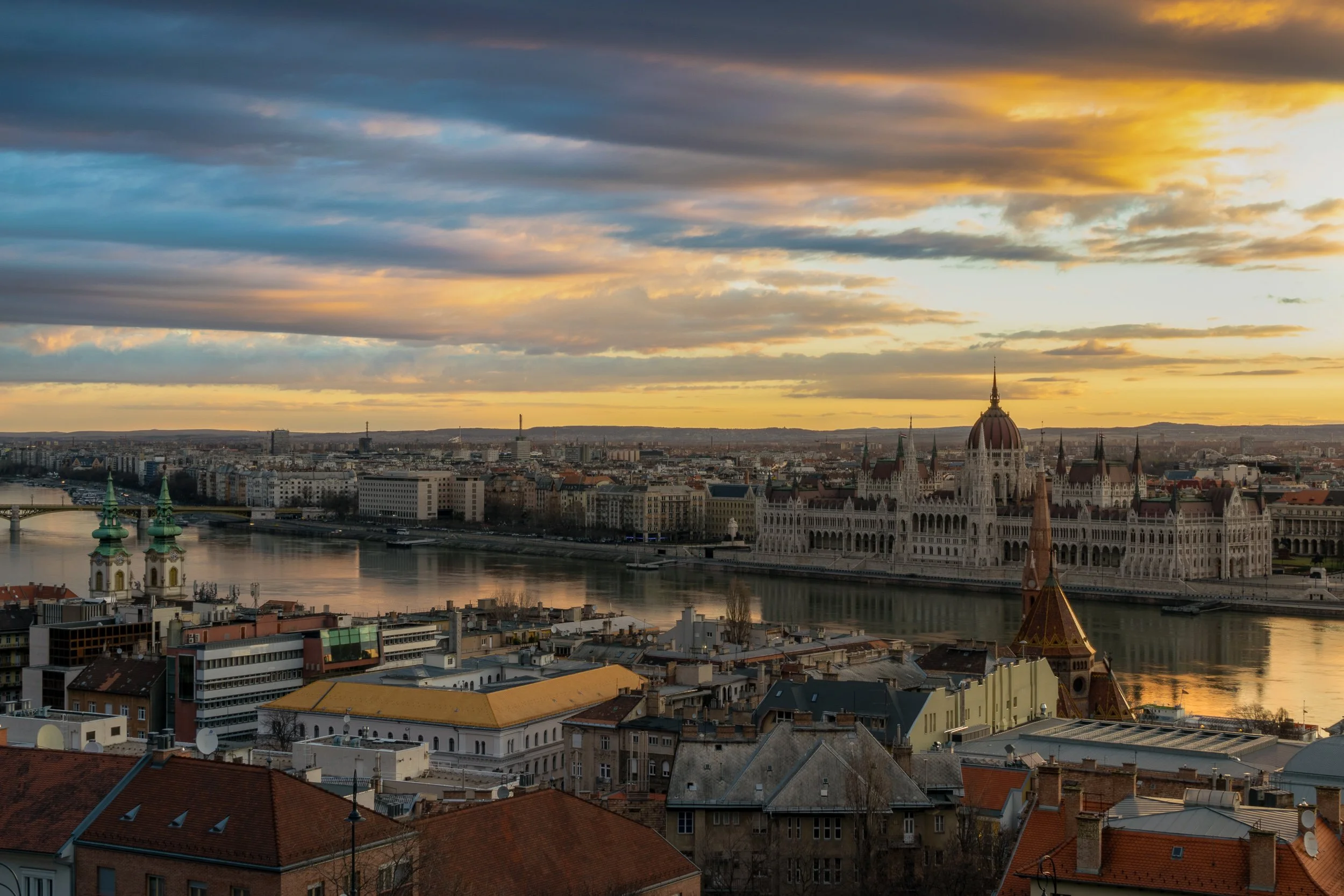 Budapest panoramic at sunset, Danube River and Hungarian Parliament building lit in orange light.
