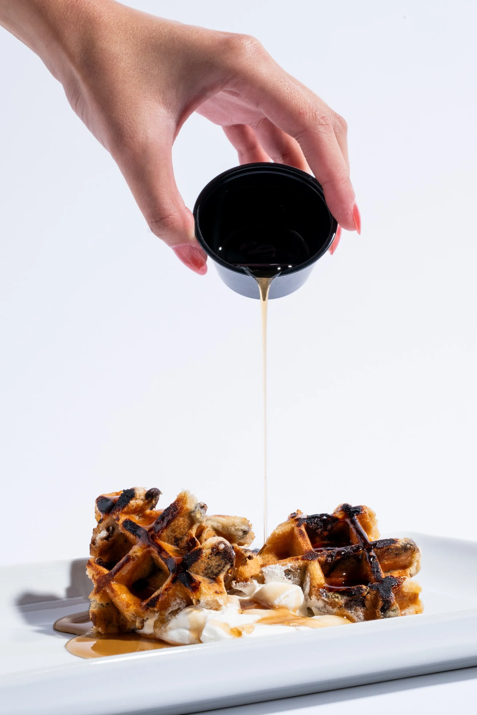 Commercial food photography showing hand pouring syrup from a small pitcher over Belgian waffles, brunch restaurant menu photography Kansas City
