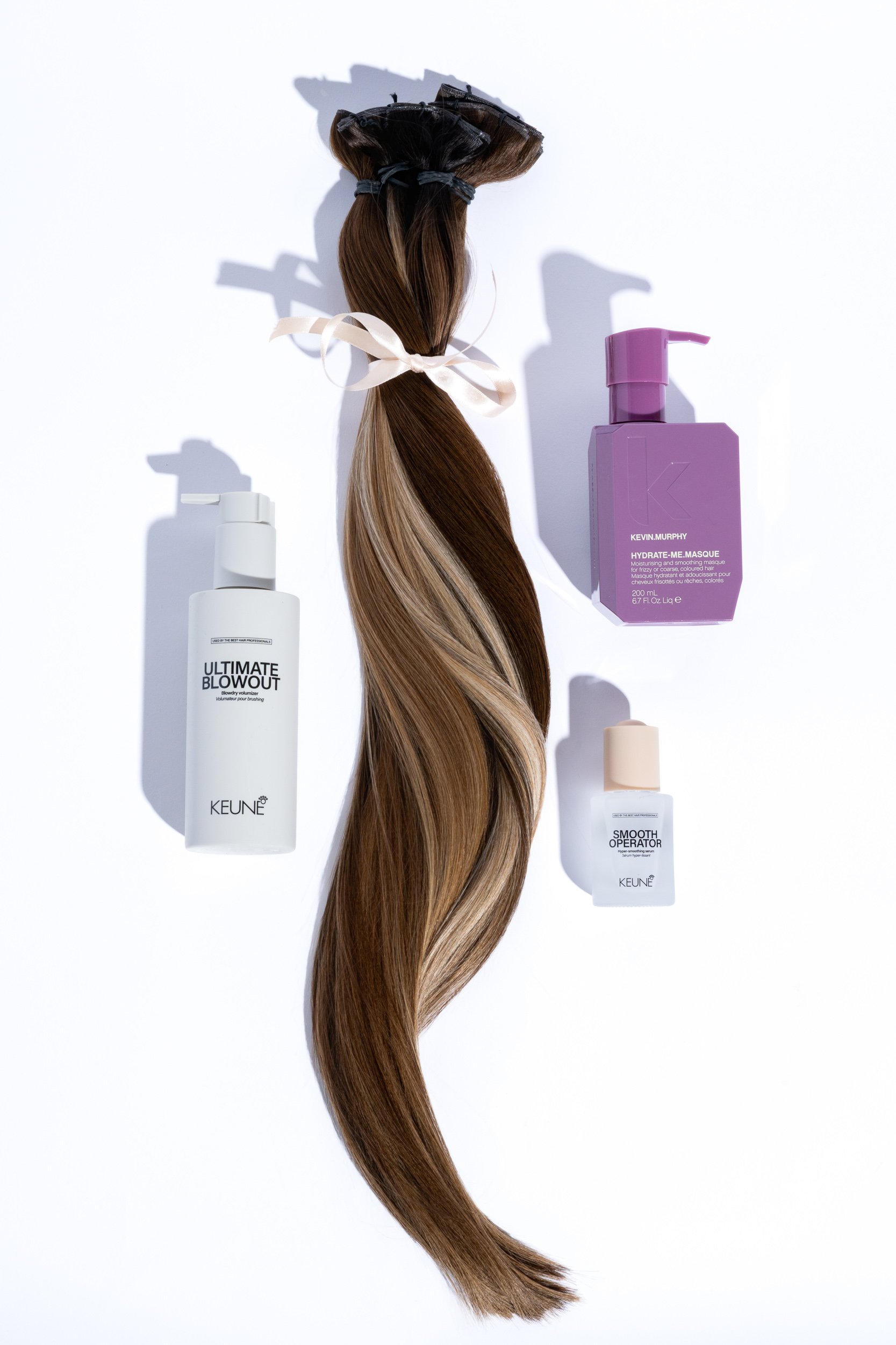 Hair extension with ribbon bow styled alongside Keune hair care products on white background