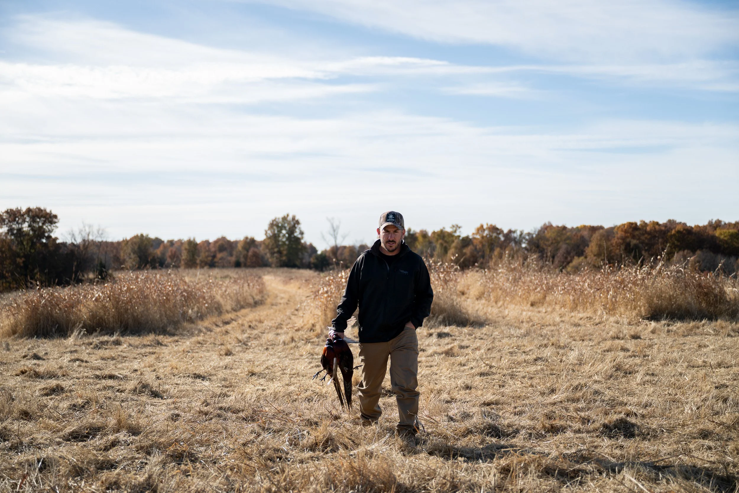 Kennel manager Eric Thiessen walks through an autumn field at Habitat Flats carrying a pheasant.