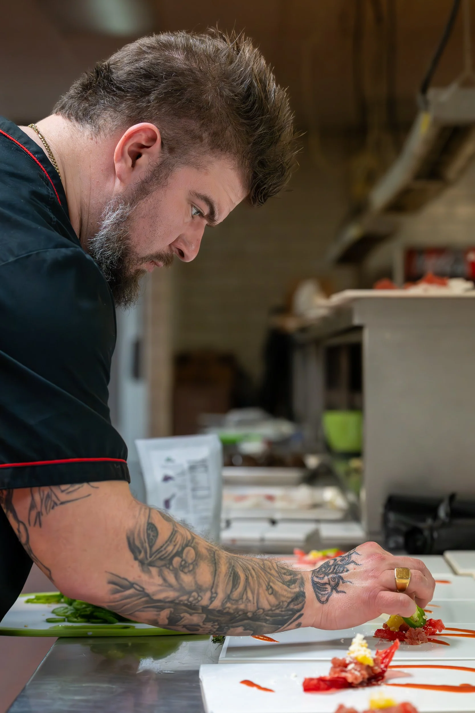 Chef in black apron focused on plating food on a white surface in a professional kitchen