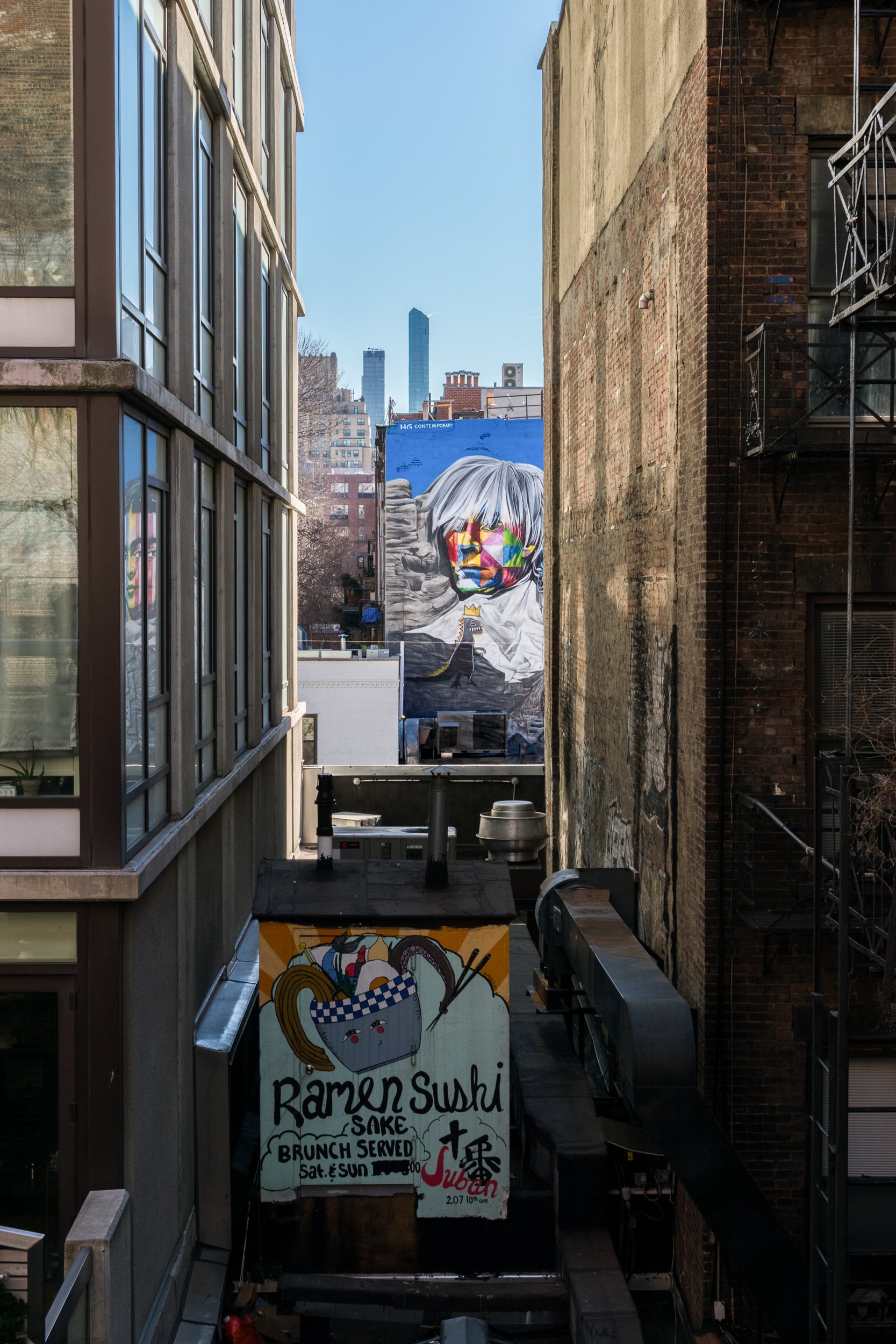 New York City alley with large face mural, fire escapes, and street signage below.