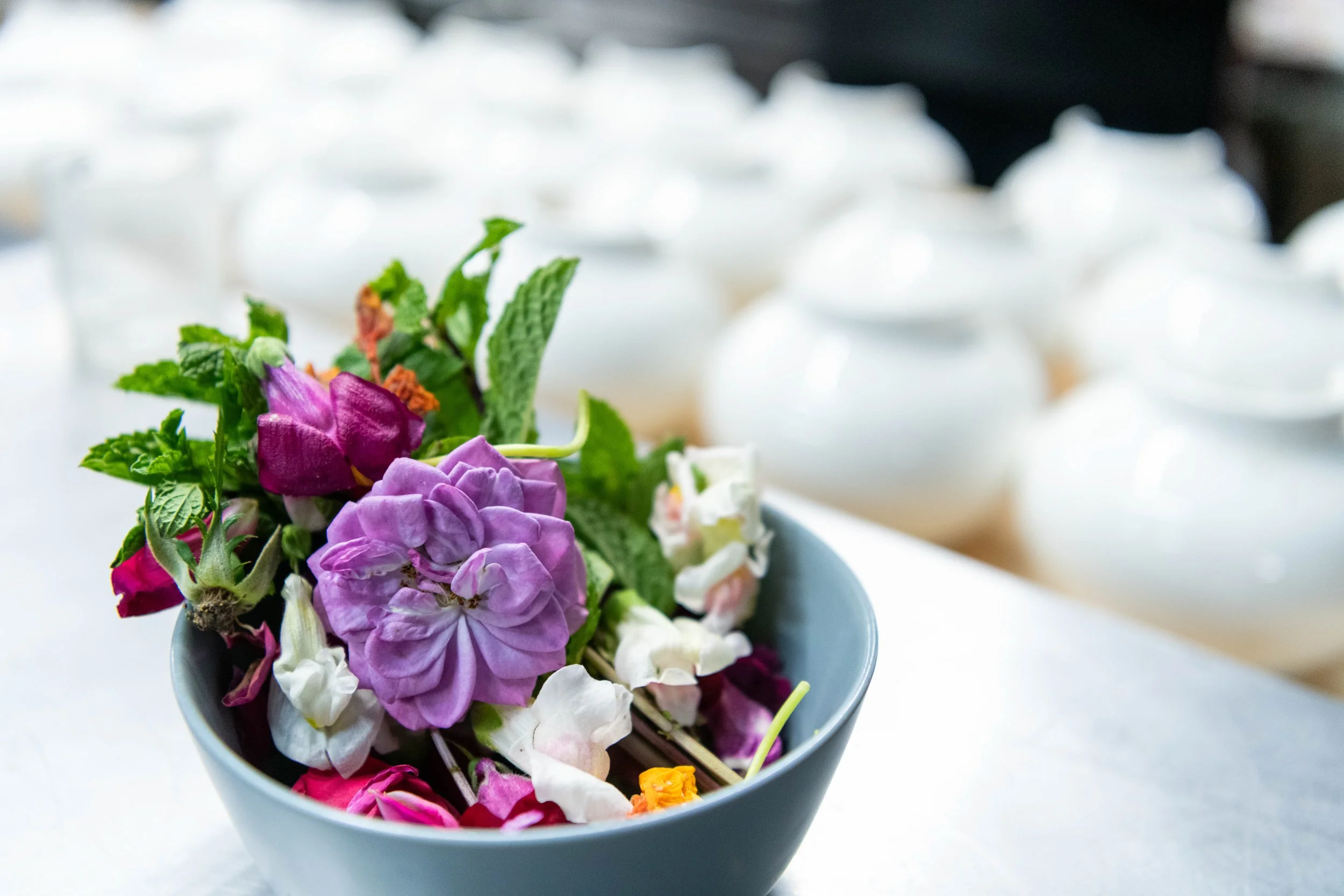 Bowl of edible flowers and herbs on stainless prep surface, fine dining ingredient sourcing photography
