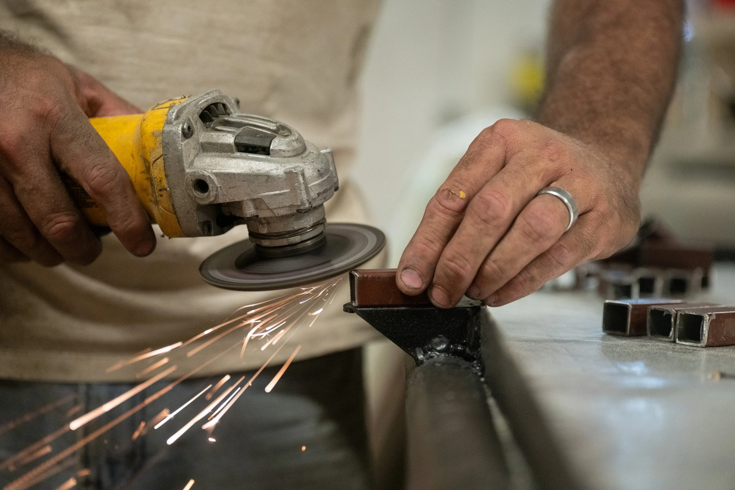 Close-up of hands running an angle grinder along a steel frame, sparks flying