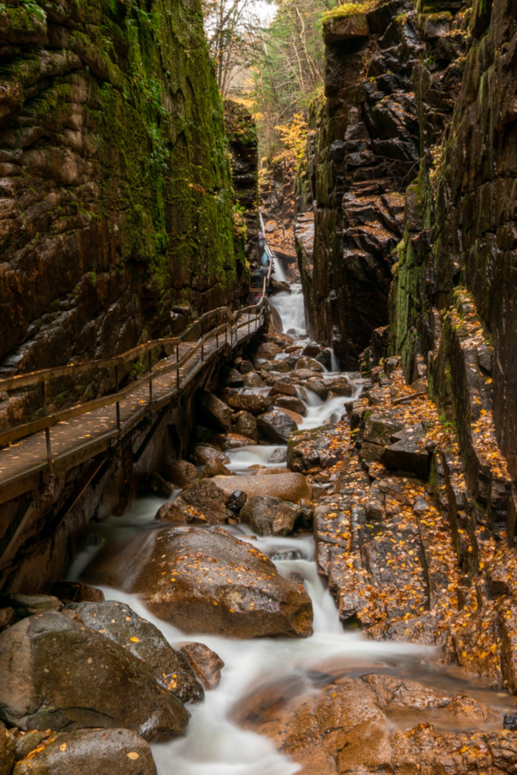 Flume Gorge, New Hampshire — narrow rock canyon with waterfall, rushing stream, wooden boardwalk, and fall foliage.