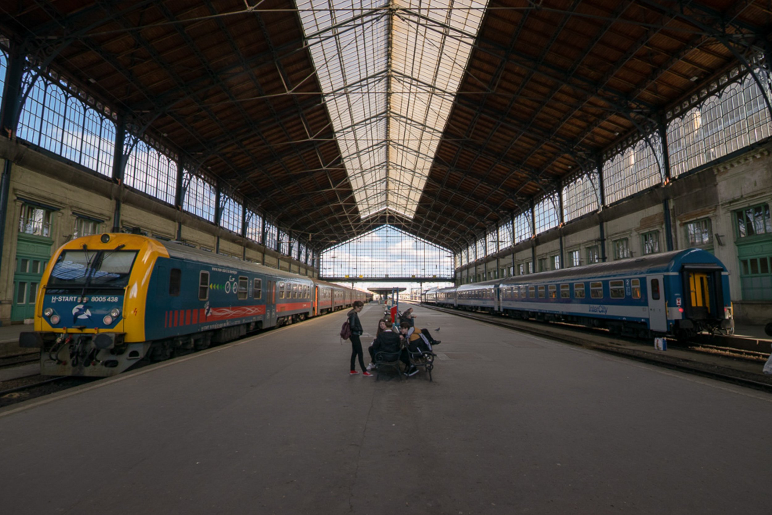 Budapest Keleti train station interior, yellow and blue train on the platform, iron and glass roof vaulting above.