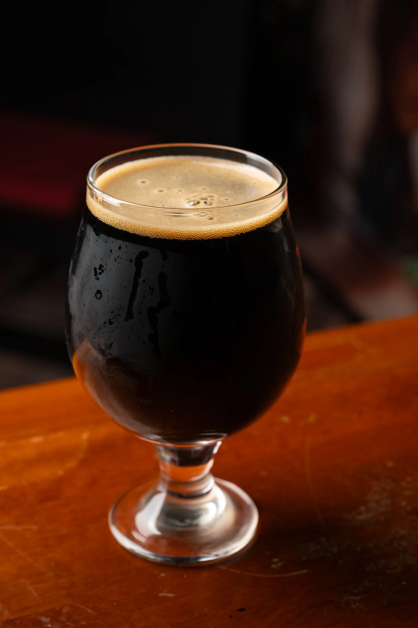Dark stout in tulip glass on wood bar, craft brewery beer photography Kansas City
