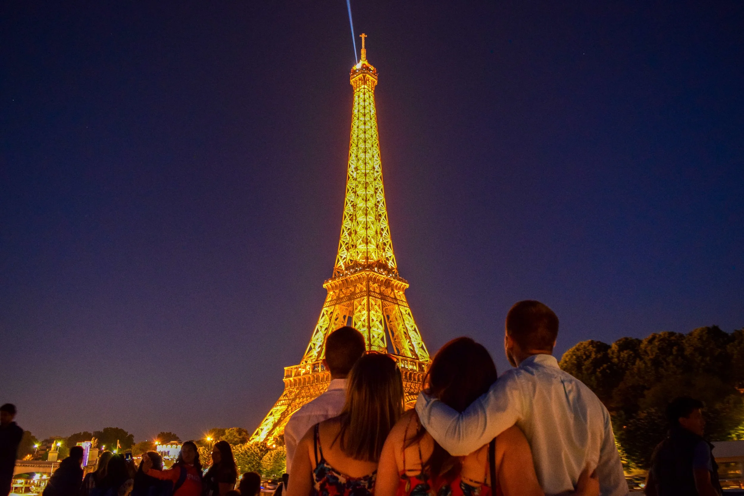 Eiffel Tower illuminated at night in Paris, France, crowds of visitors watching from the Champ de Mars.