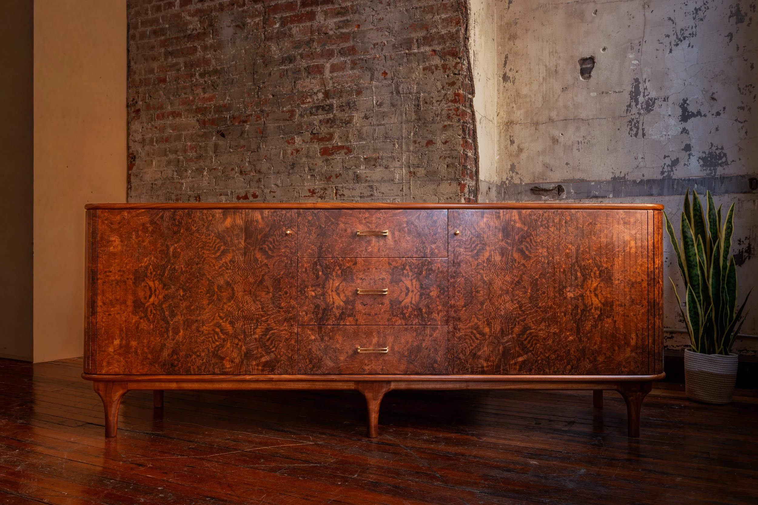 Mid-century modern wood sideboard against an exposed brick wall with hardwood floors