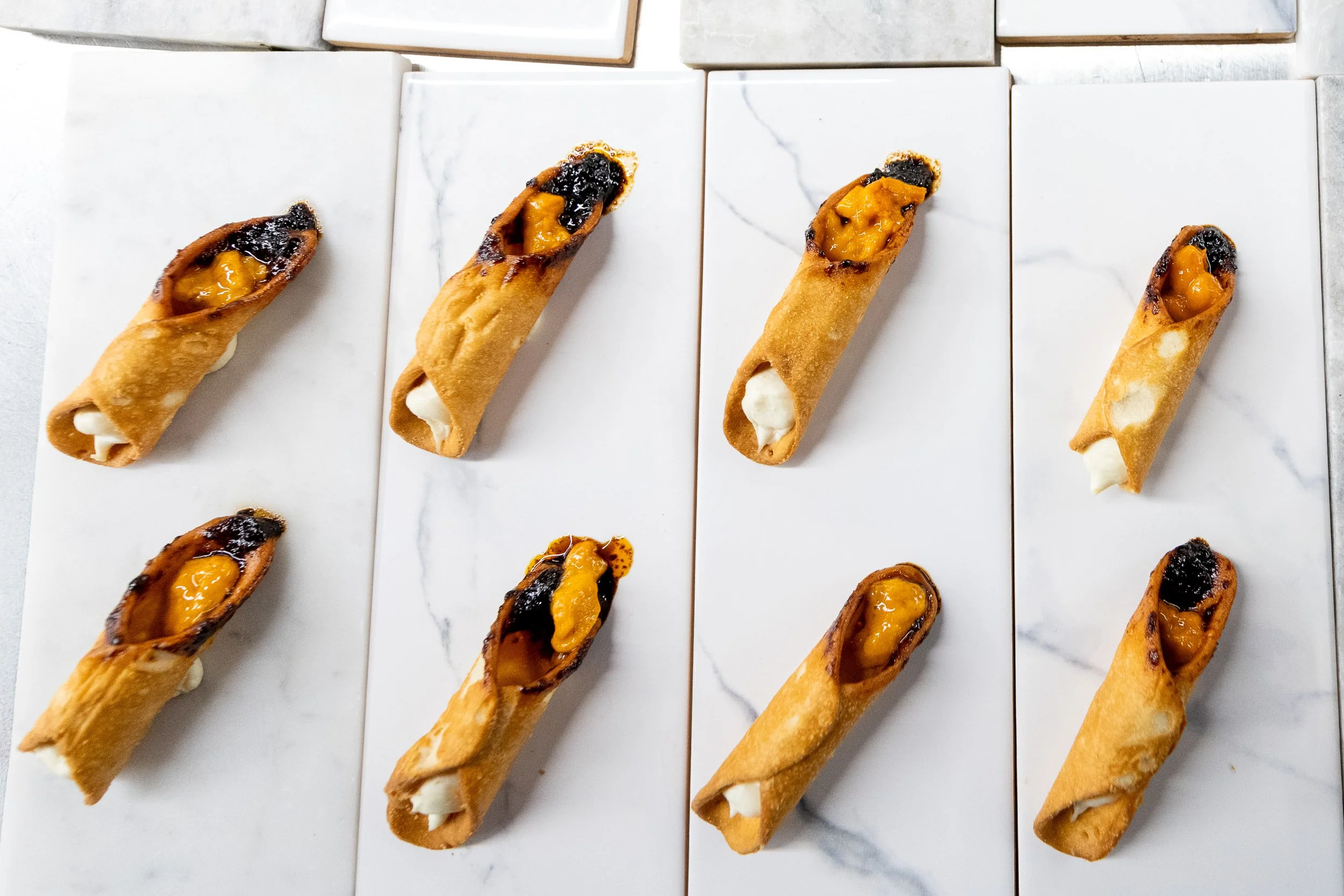 Phyllo pastry rolls arranged in rows on white marble, fine dining appetizer preparation
