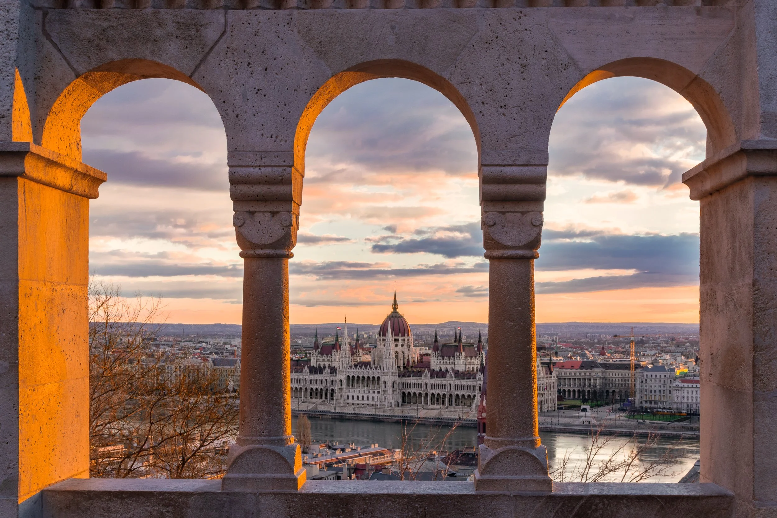 Hungarian Parliament building framed through arches at Fisherman's Bastion, Budapest, at sunset.