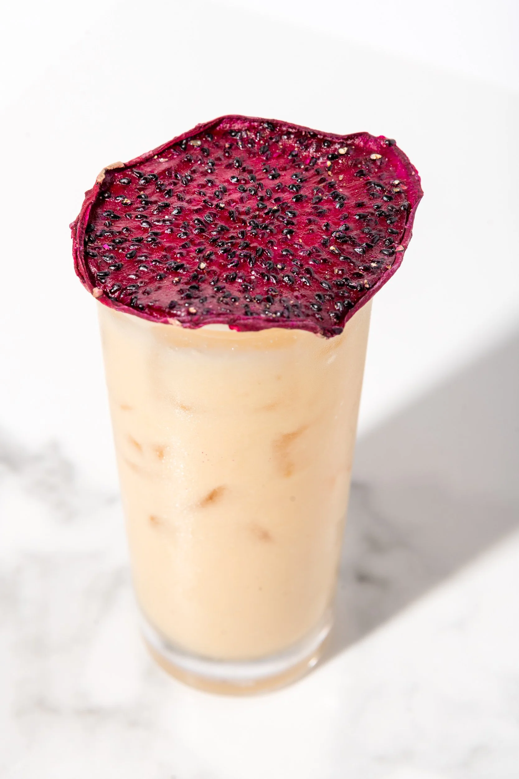 Iced latte topped with dehydrated dragon fruit chip, specialty coffee drink photography
