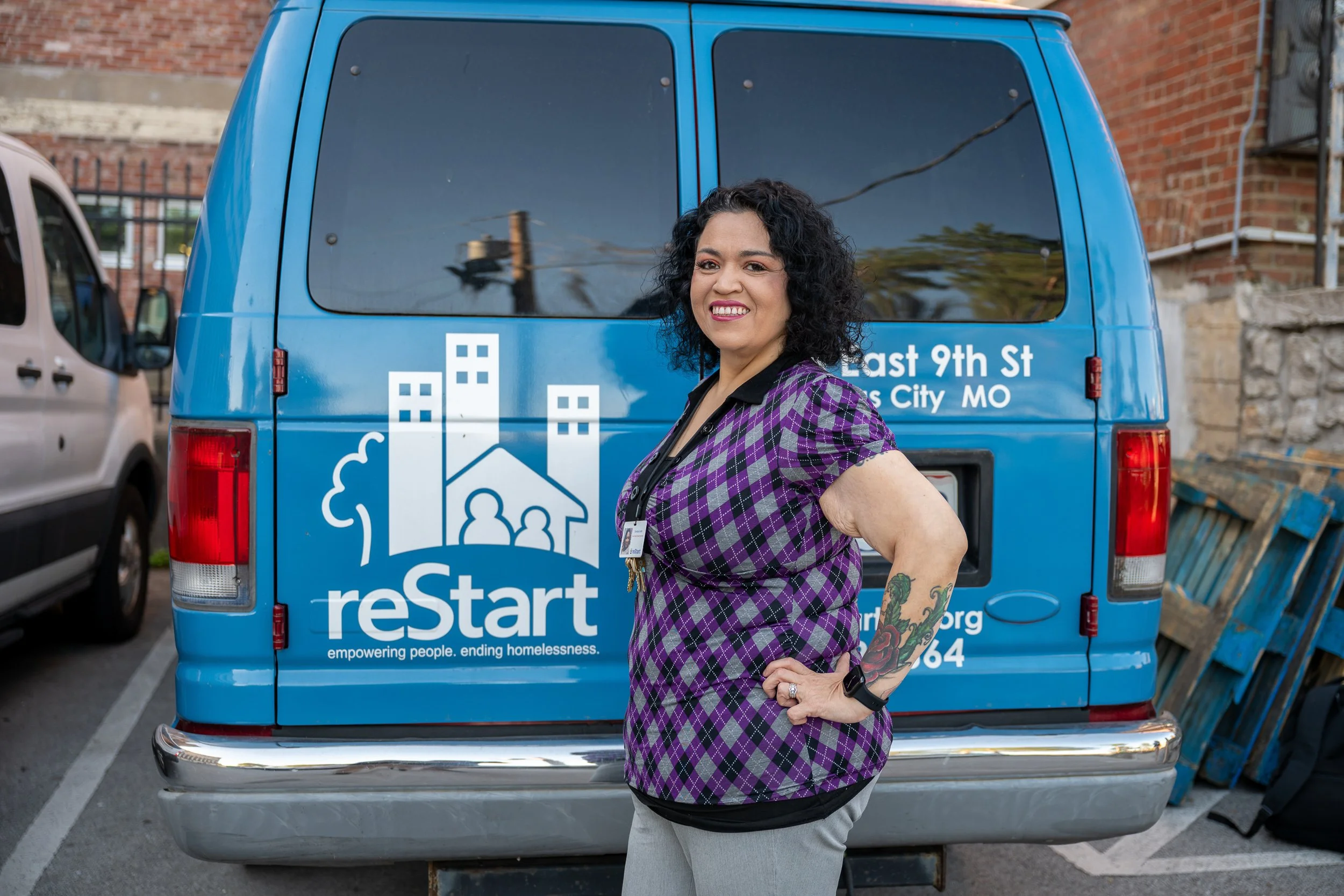 Woman smiling in front of a blue reStart branded van in an urban alley setting