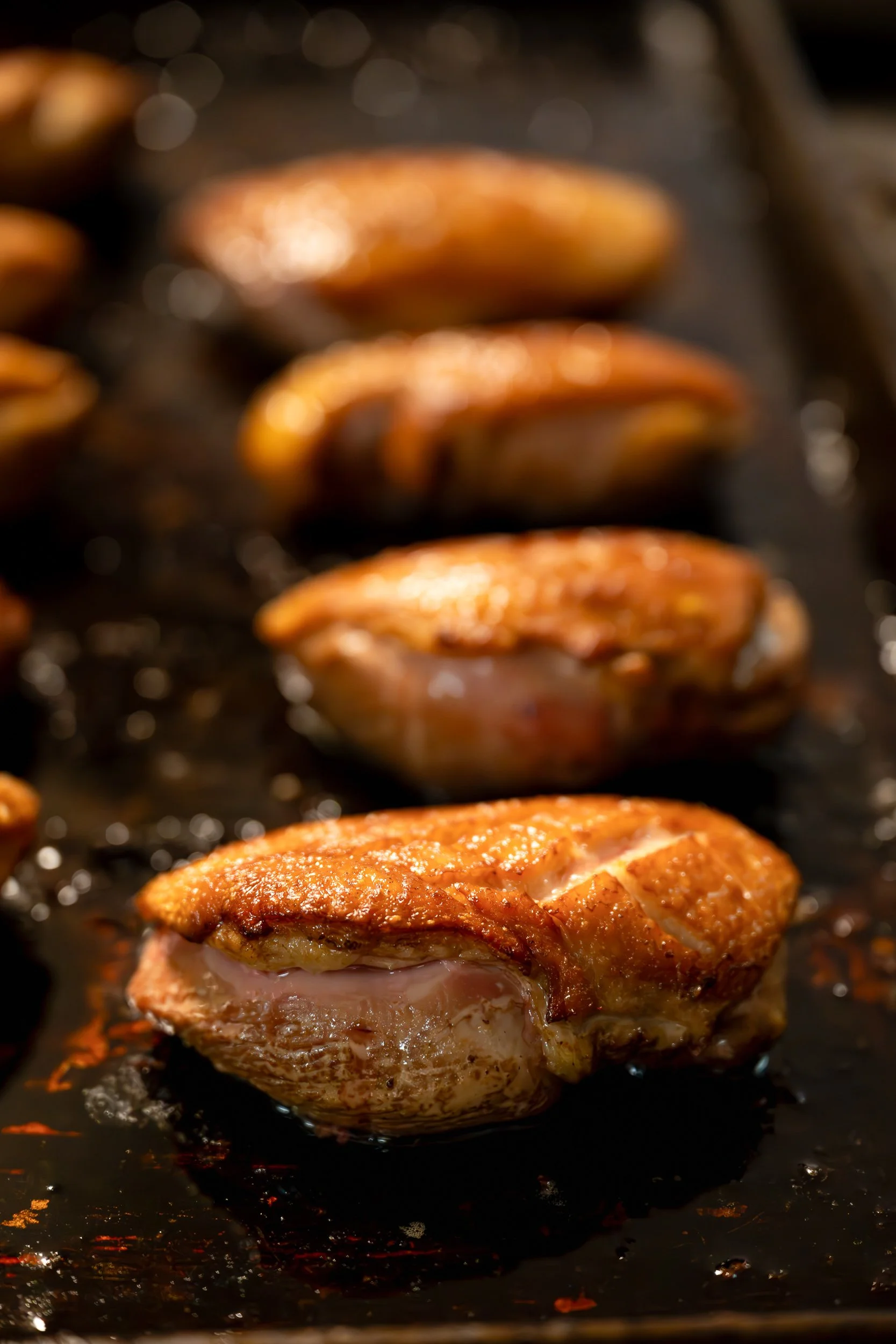 Row of scored duck breasts resting on a dark grill pan, restaurant kitchen food photography