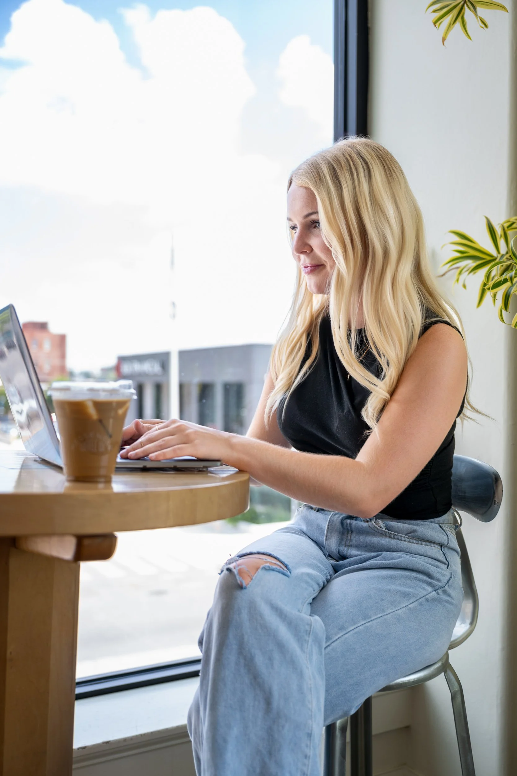 Small business owner working on a laptop at a coffee shop window with natural light