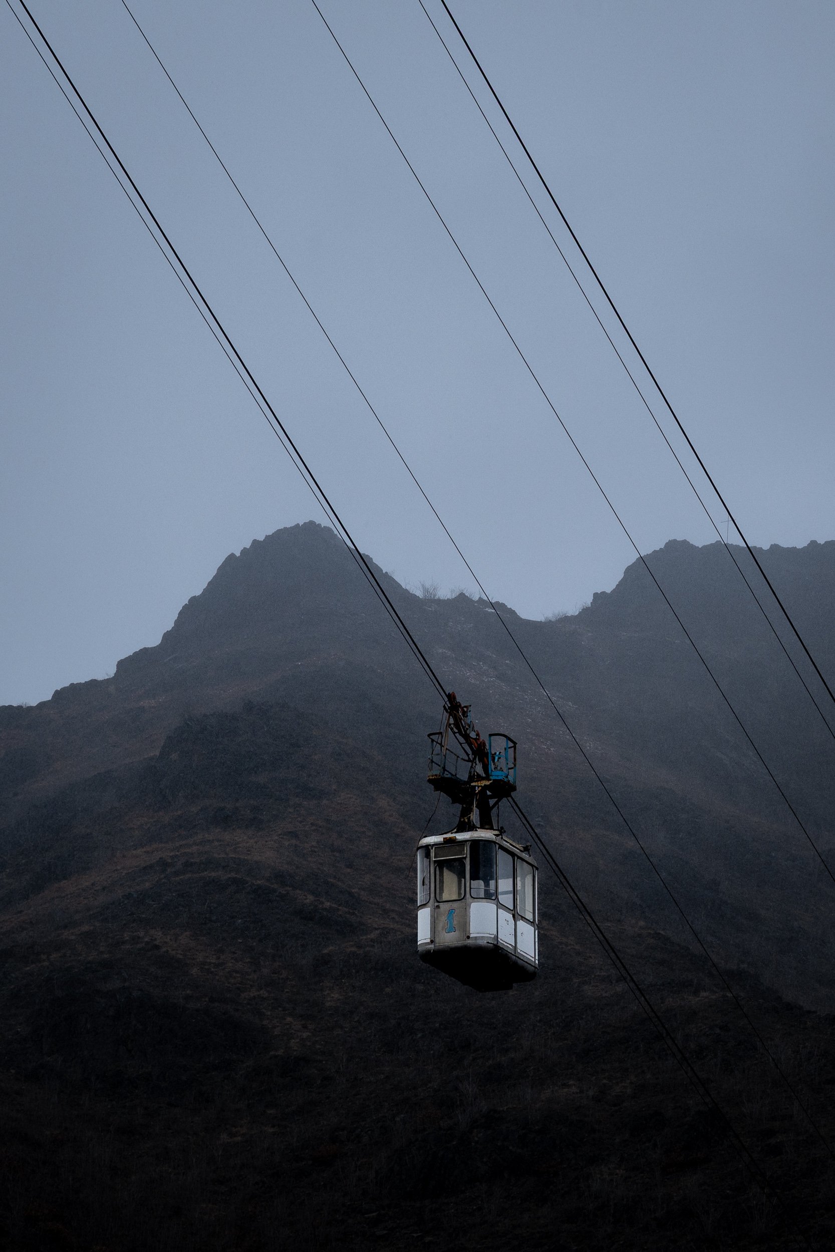 A weathered cable car rests motionless against the mountains of Georgia, surrounded by fog and fading infrastructure.