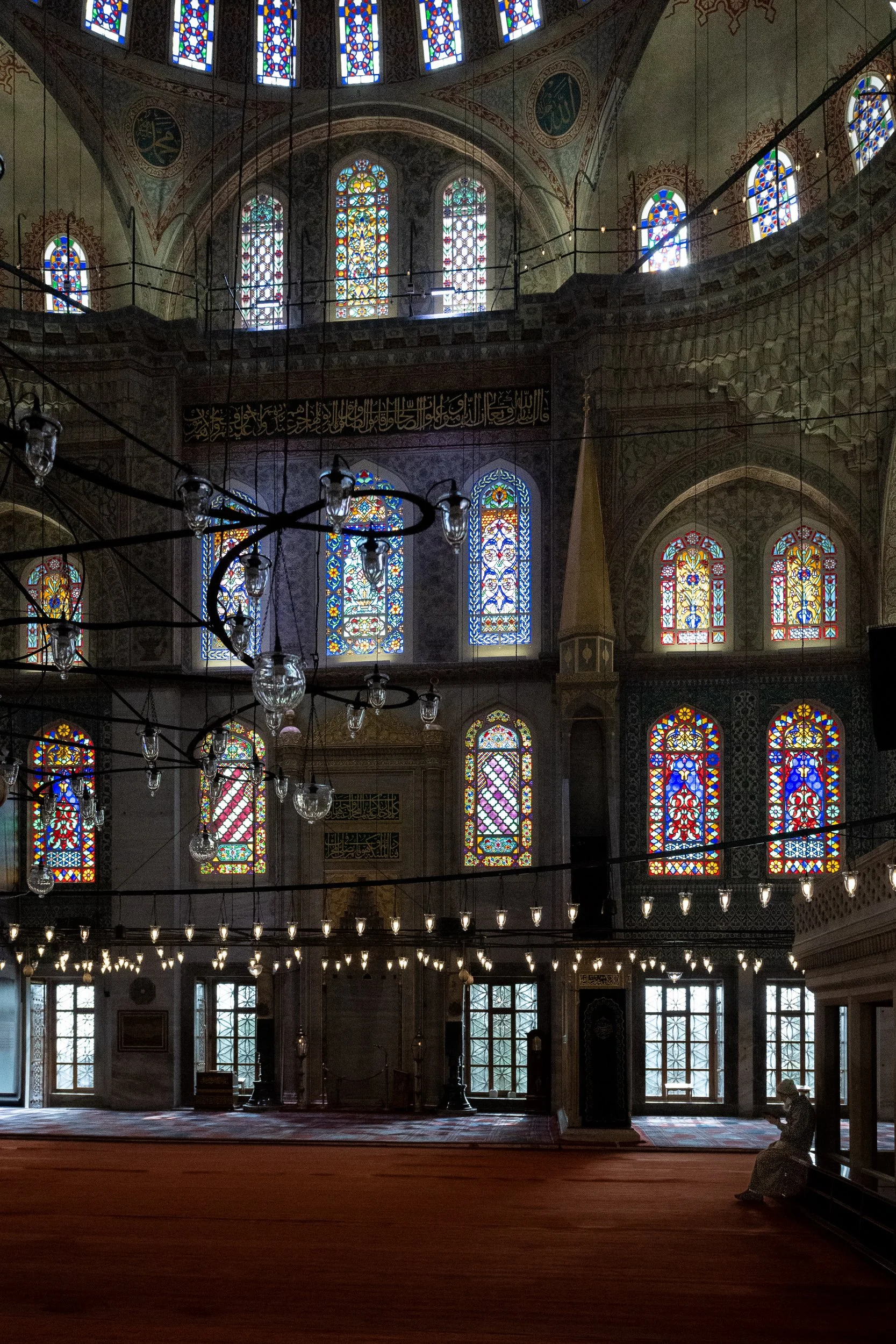 Sunlight filters through stained glass as a lone worshipper sits quietly beneath the soaring architecture of an Ottoman mosque.
