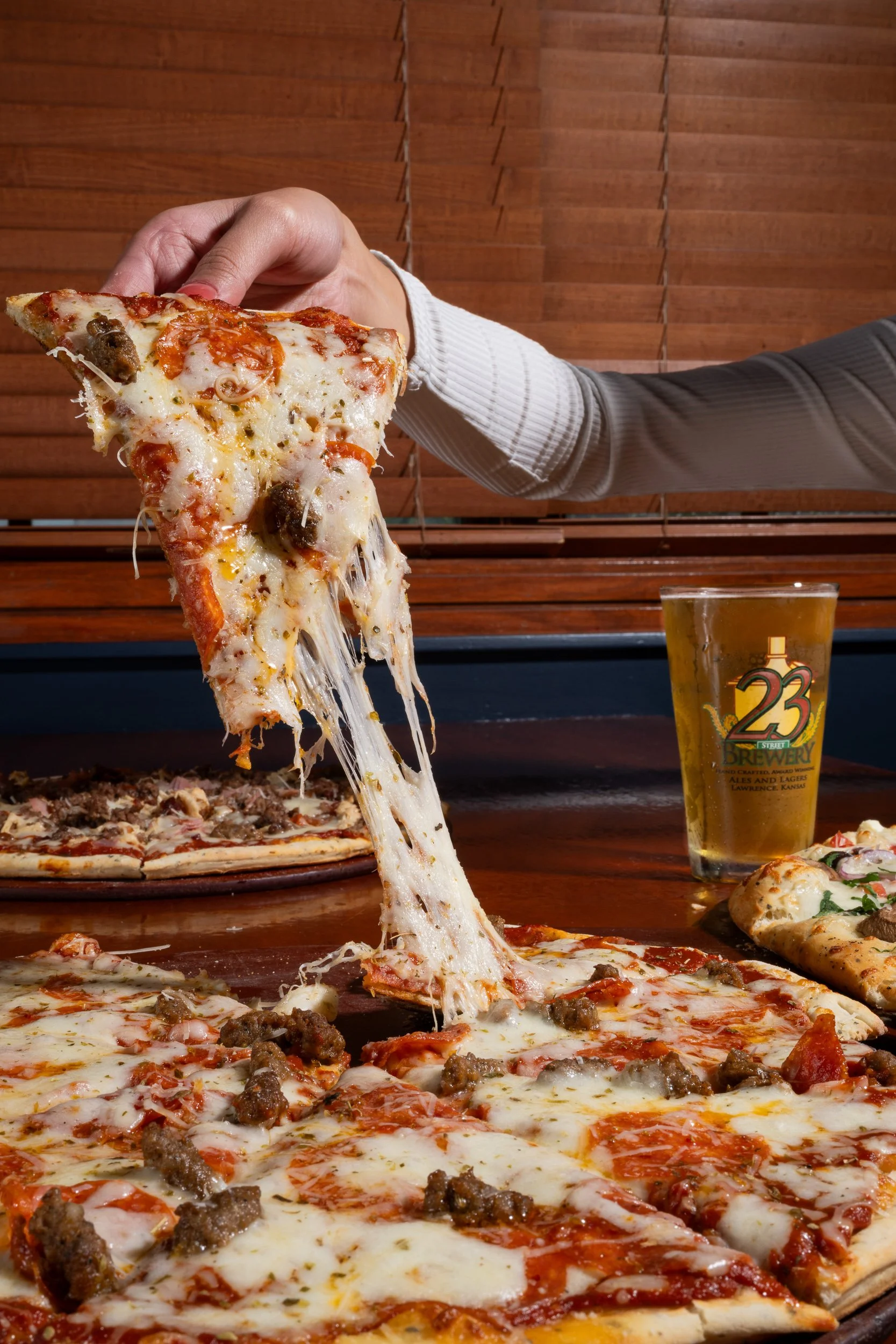 Hand pulling cheese pizza slice with draft beer, Kansas City brewery food and beverage photography
