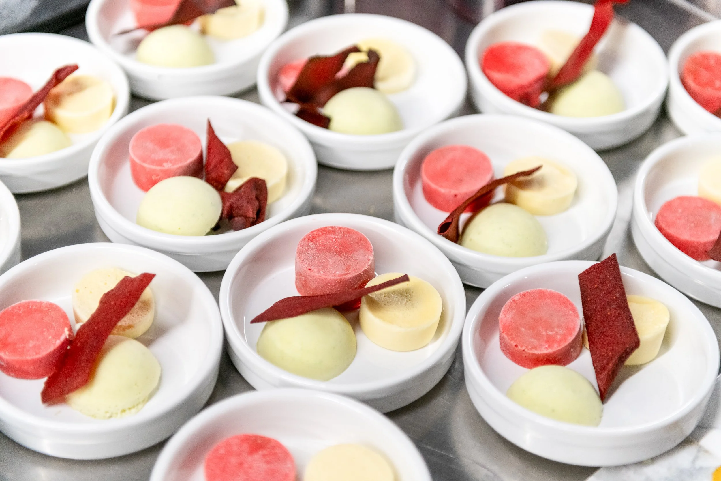 White ramekins filled with pink and white dessert discs prepared for dinner service