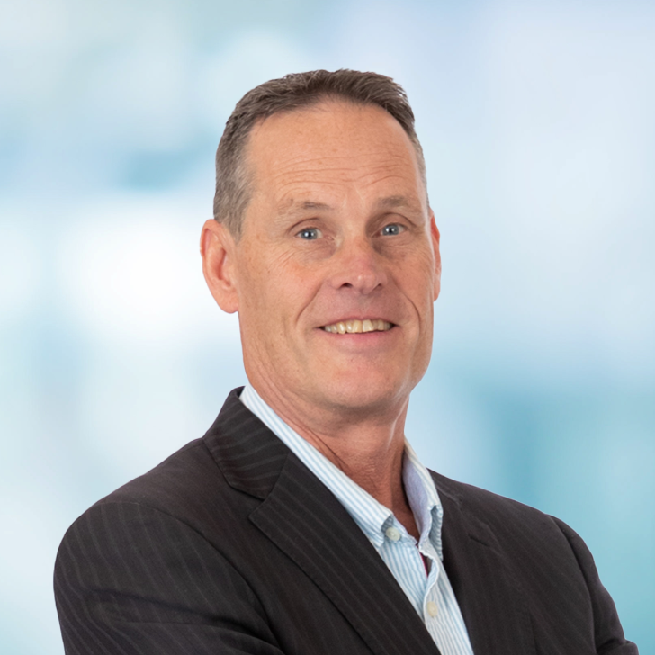 Smiling middle-aged man in a business suit standing against a blurred professional background.