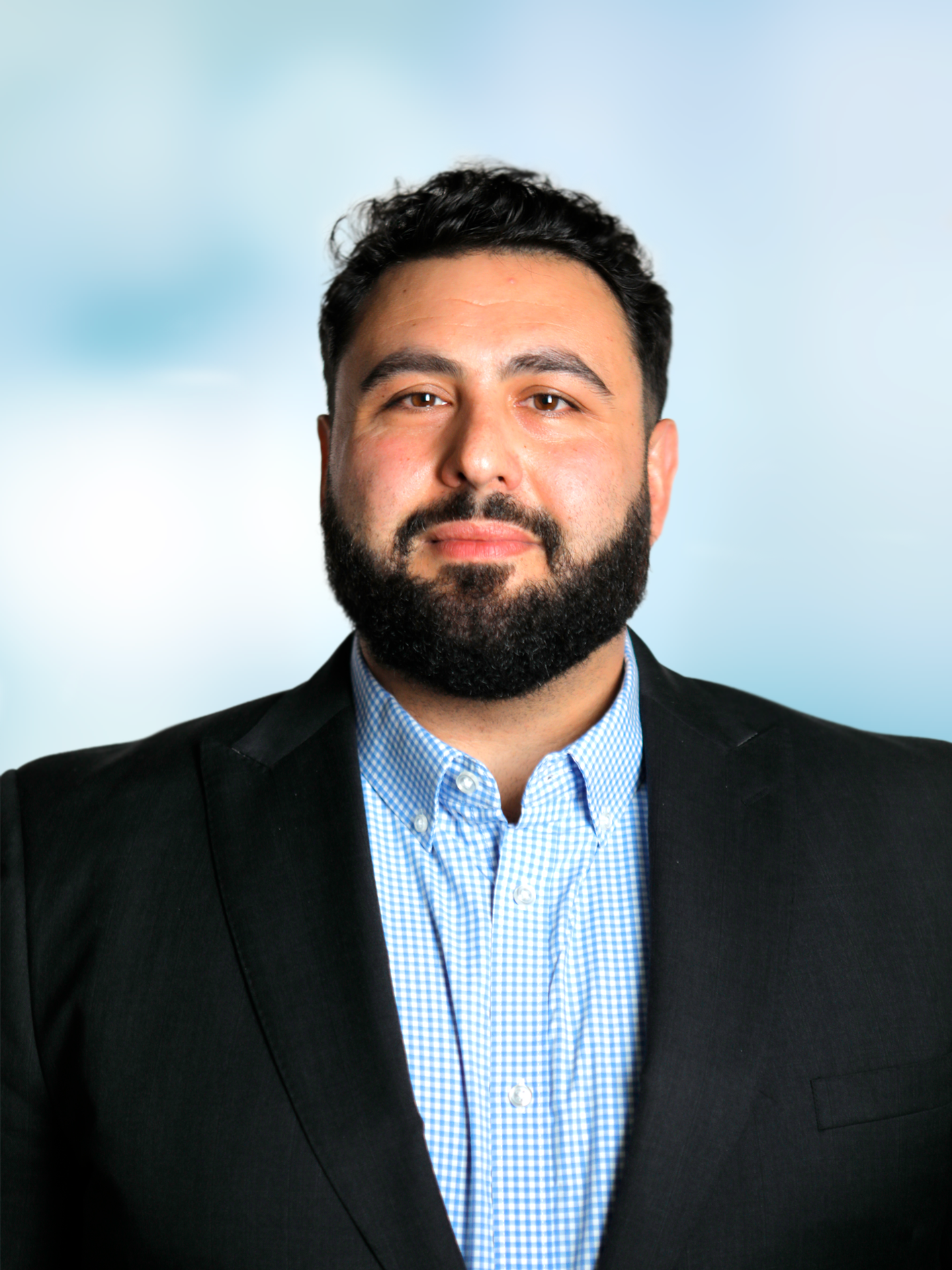 Professional headshot of a man with a  beard in a black suit and checked shirt