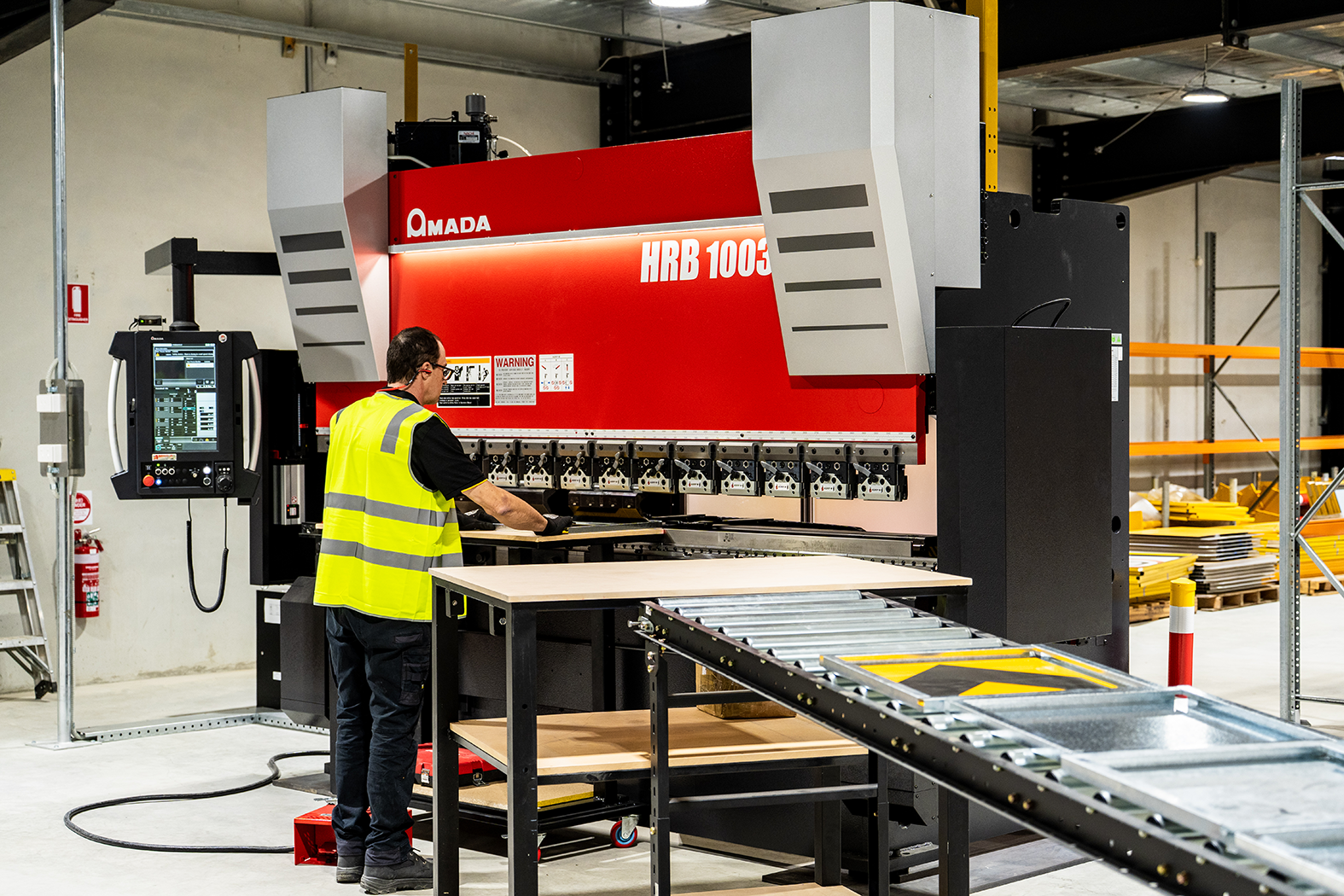 A worker operating an industrial metal bending machine in a warehouse setting.