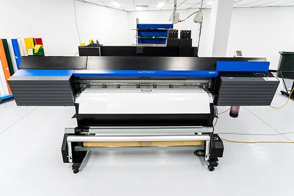 Large flatbed printer in a bright, clean workshop with shelves and tools in the background.