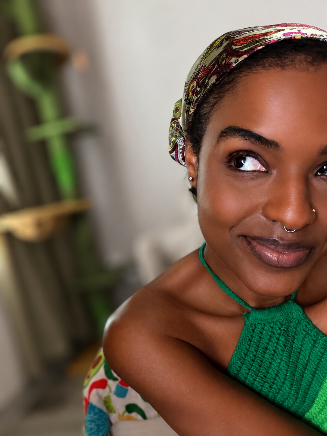 A woman with dark skin wearing a colorful headscarf and a green top, smiling and looking to her right.