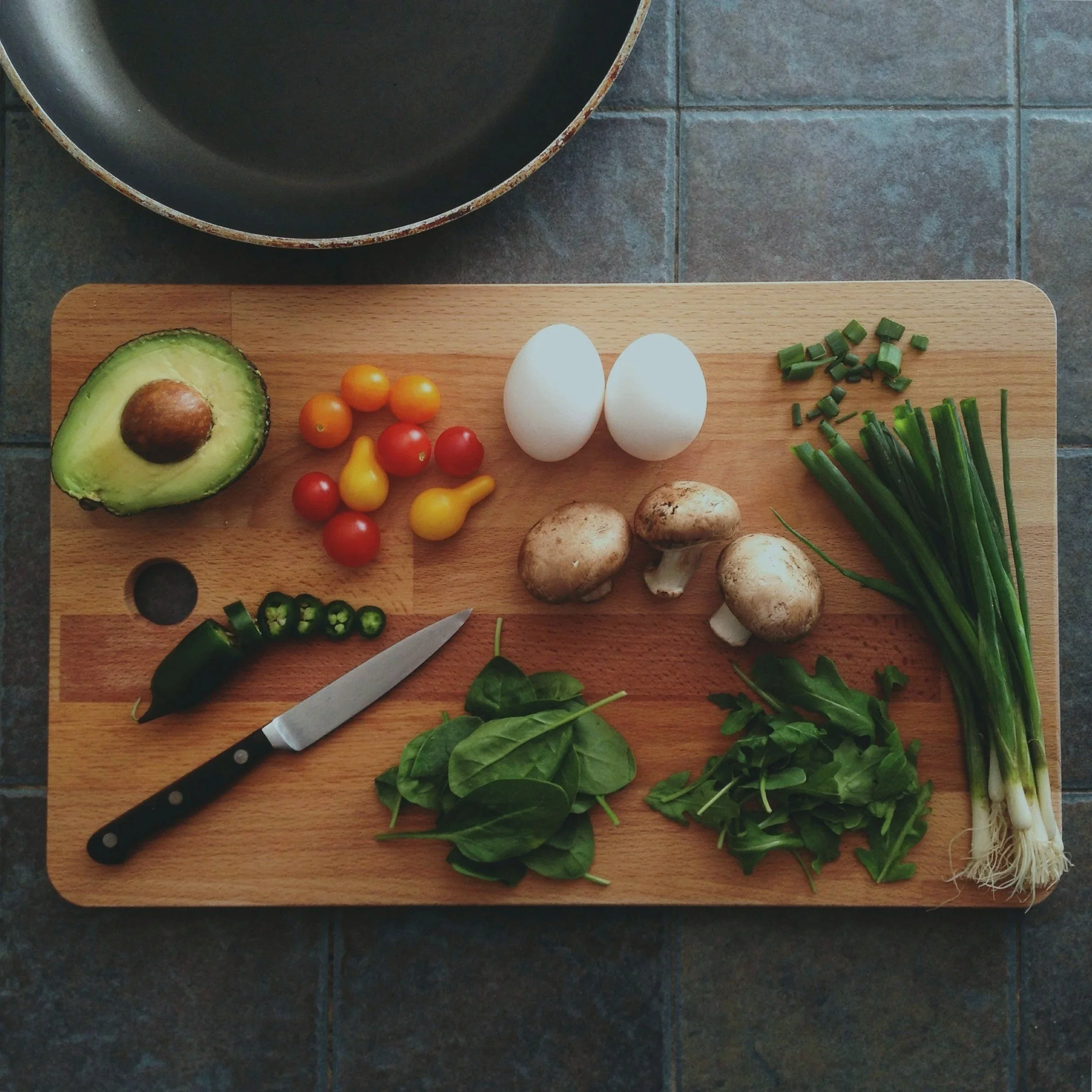 cutting board with variety of vegetables, eggs, and knife