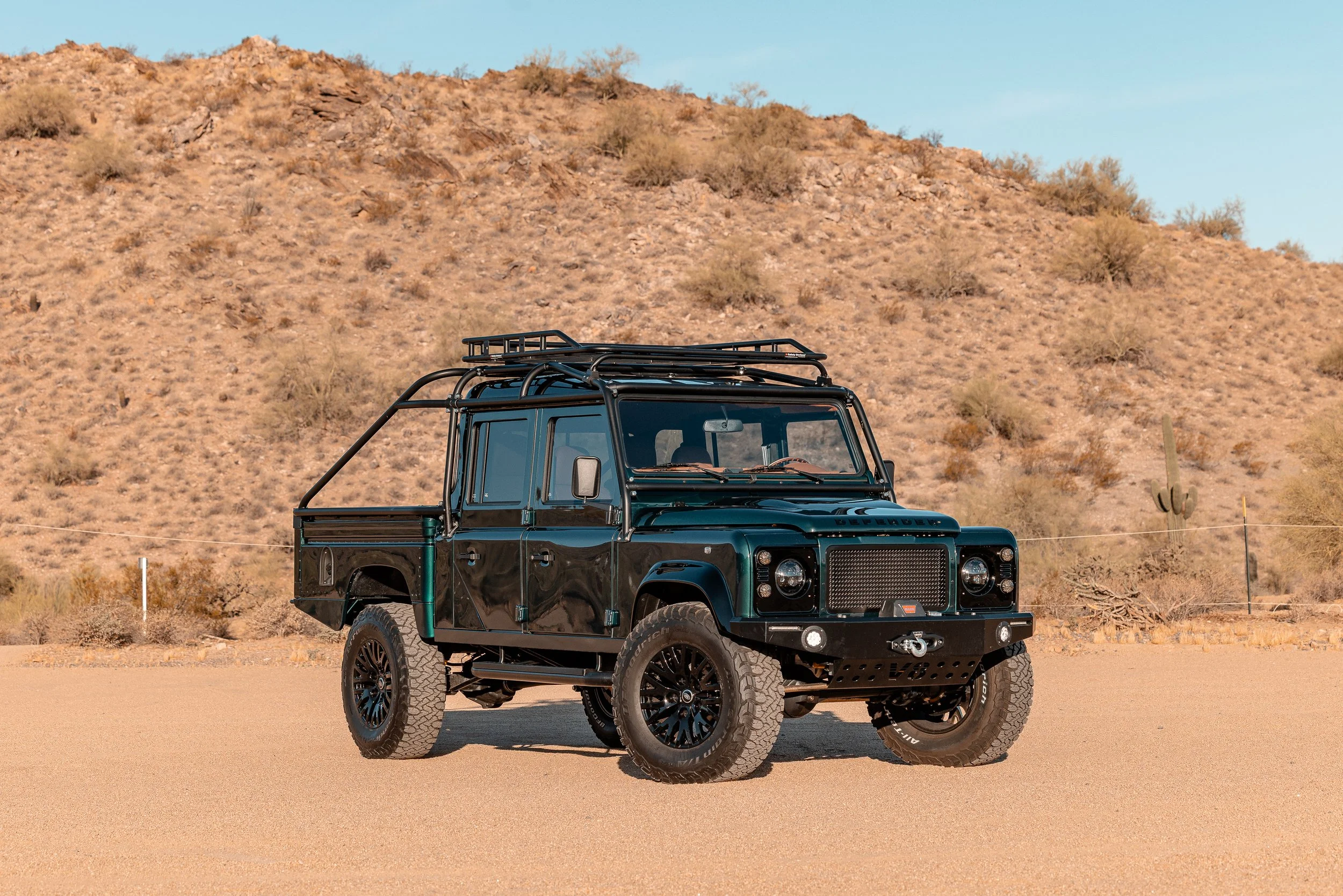 A black off-road vehicle with a roof rack parked in a desert landscape with a brown, rocky hill in the background.