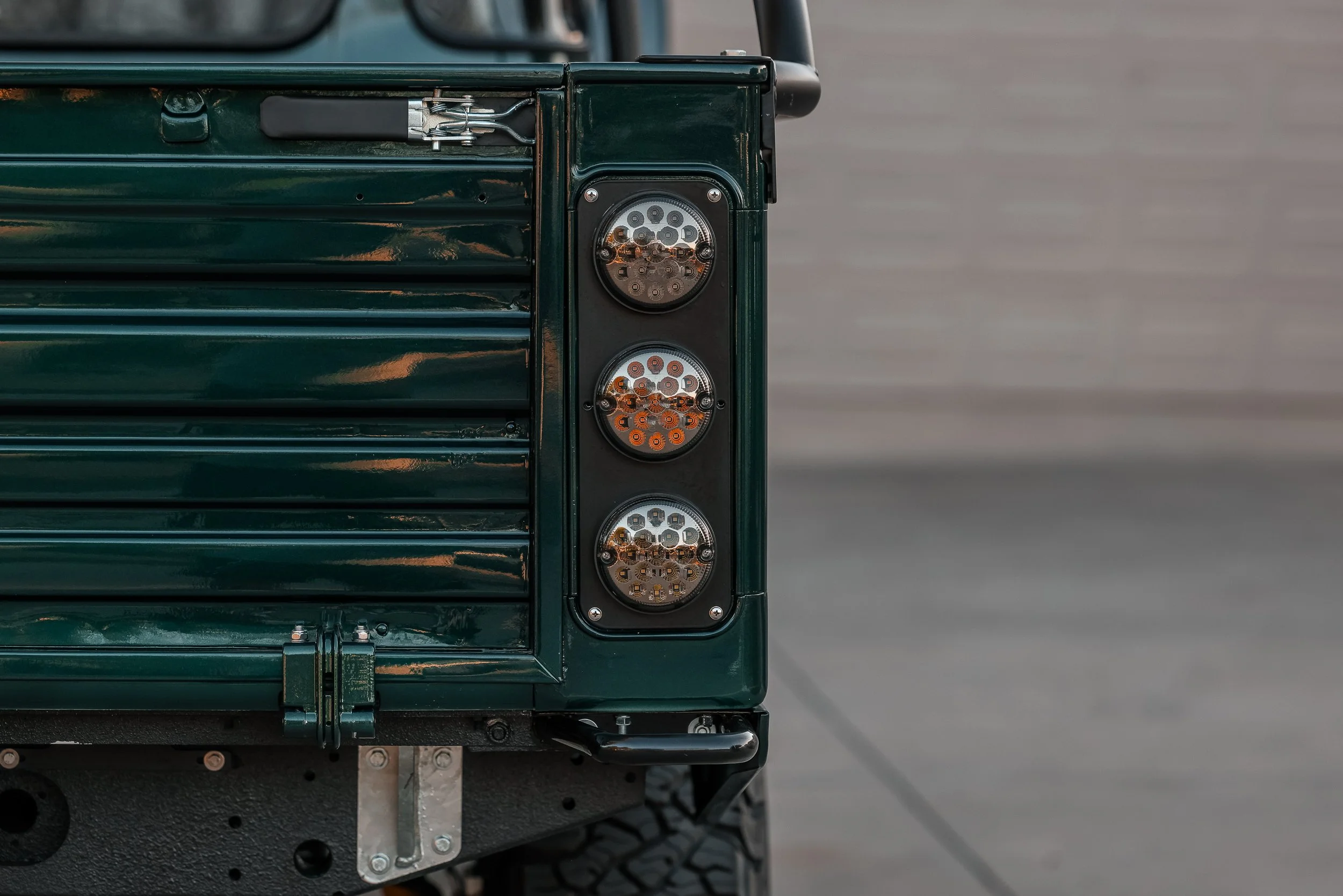 Close-up of a vehicle's rear corner with LED tail lights and a dark green body, showing some rust and mechanical parts.