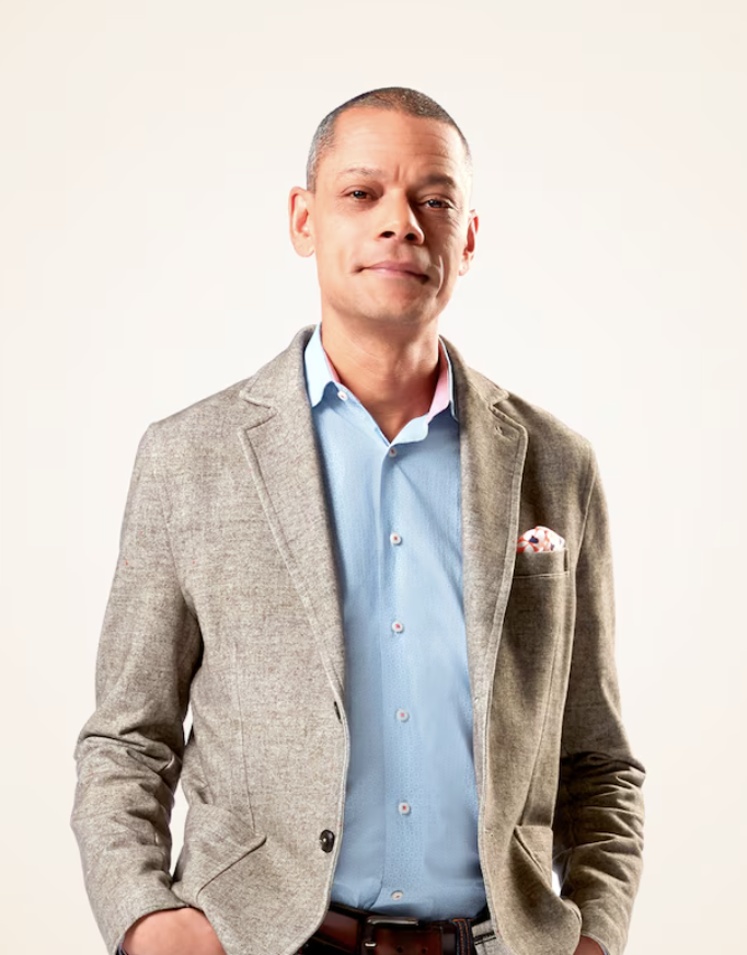 A man in a grey blazer and blue shirt standing confidently against a plain white background (Matt Galloway - CBC)