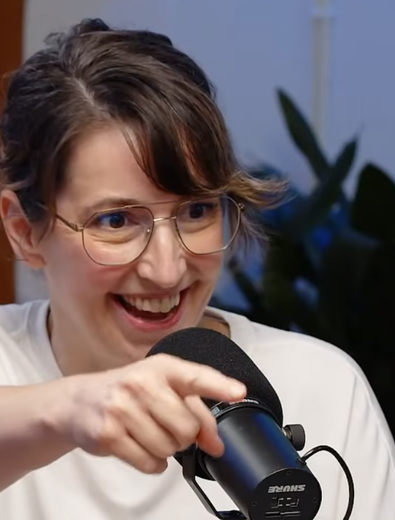 JoAnne Pearce in a white shirt smiling while talking into a black Shure microphone