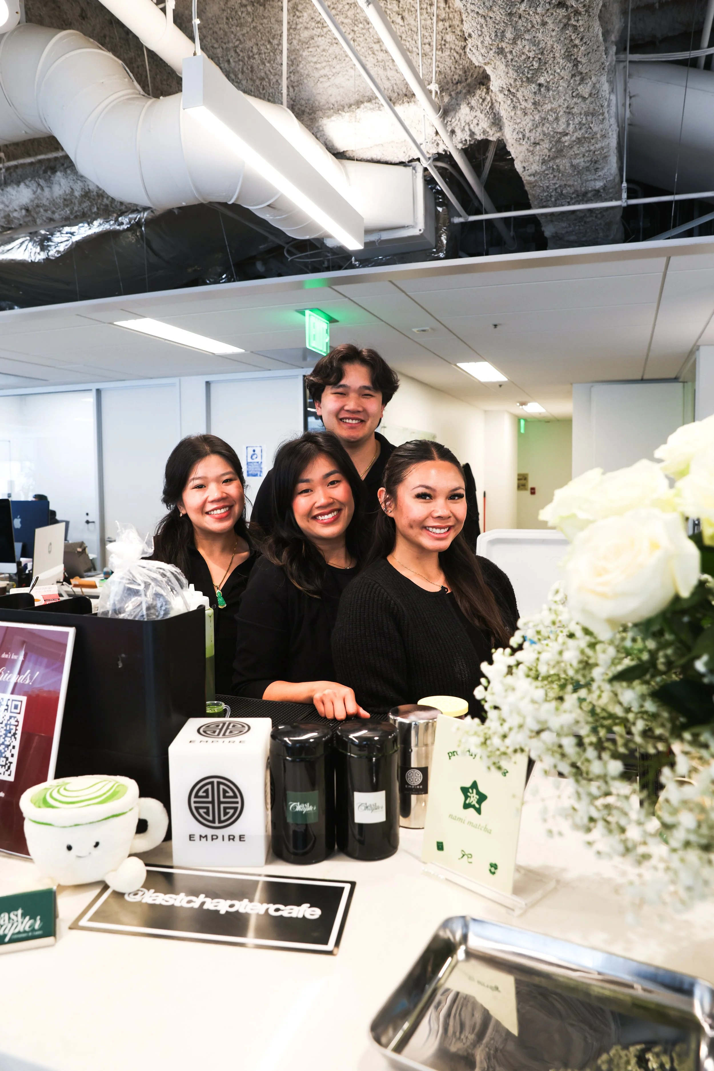 Four women smiling behind a counter at an indoor event, with products and flowers displaying on the counter. Bay Area coffee and matcha catering for corporate events, brand activations, weddings, markets, and private gatherings. Handcrafted drinks ser