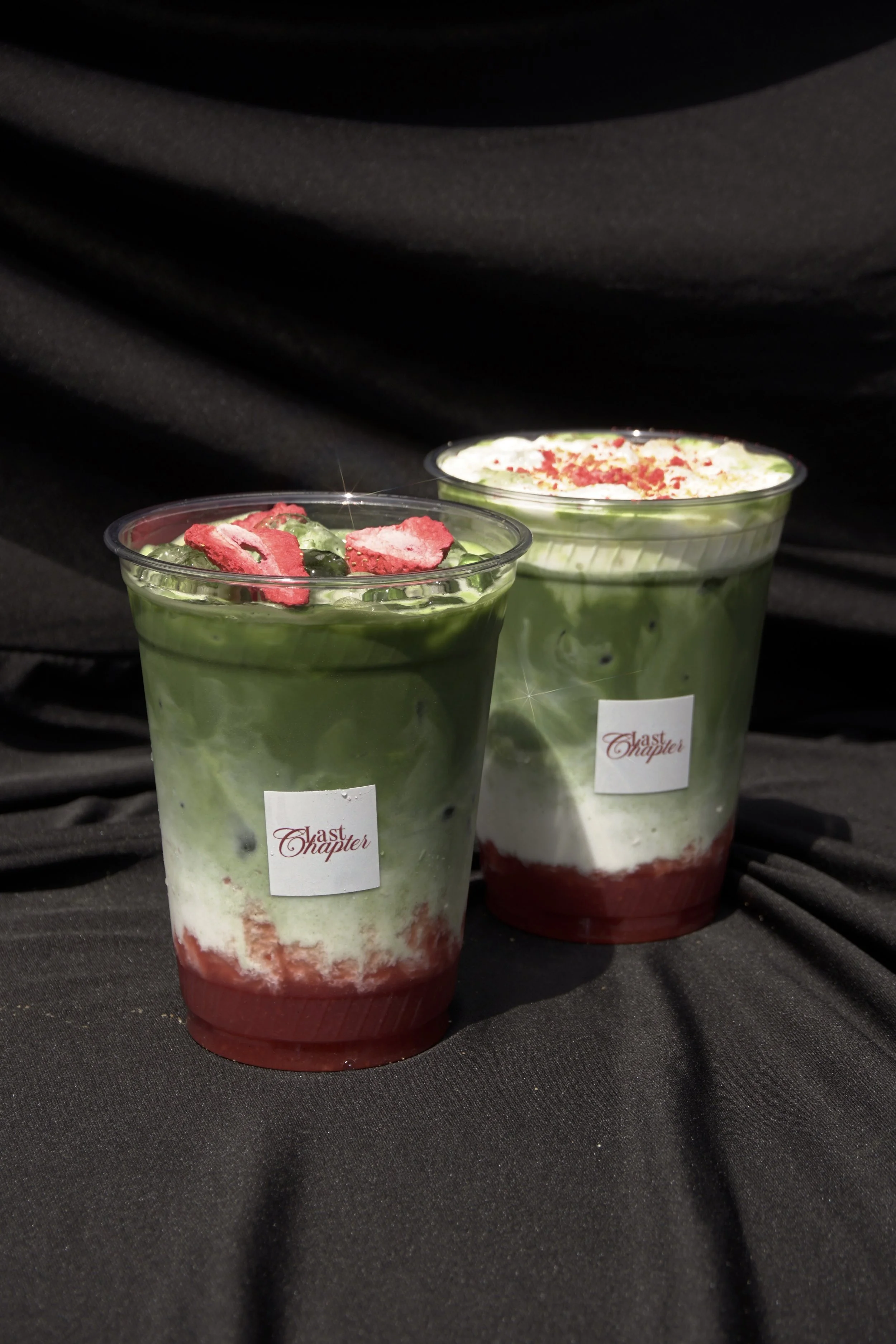 Two layered dessert cups with green, white, and red layers, topped with red decoration and sprinkles, set against a black background.