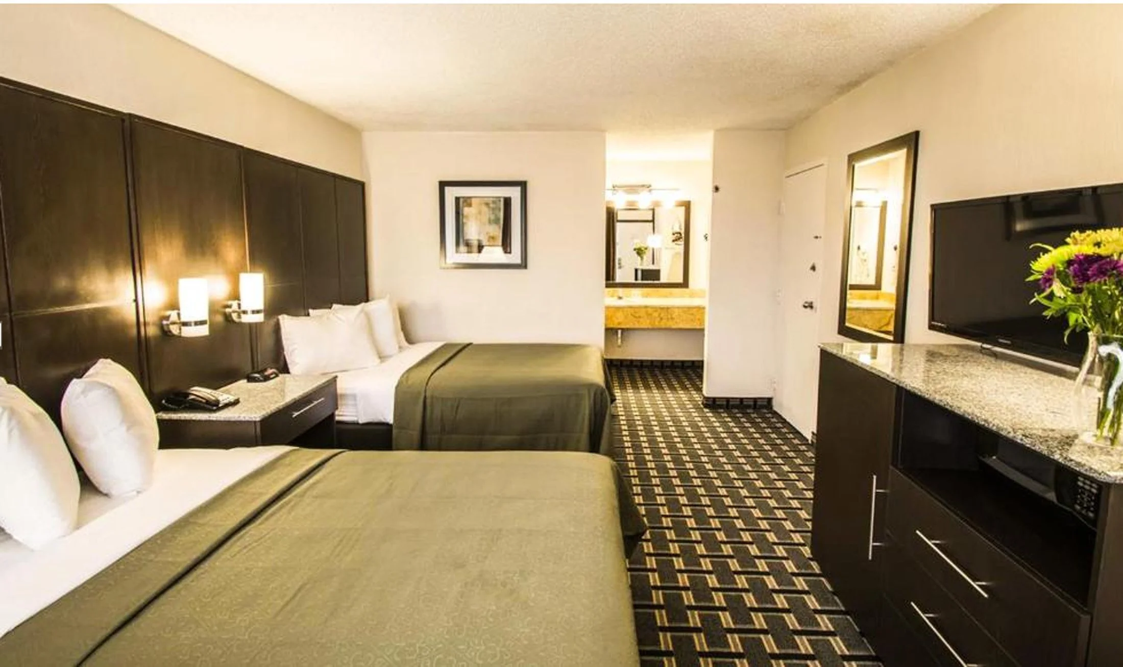 Interior of a hotel room with two beds, a flat-screen TV, a mirror, and a small vanity area in the background.