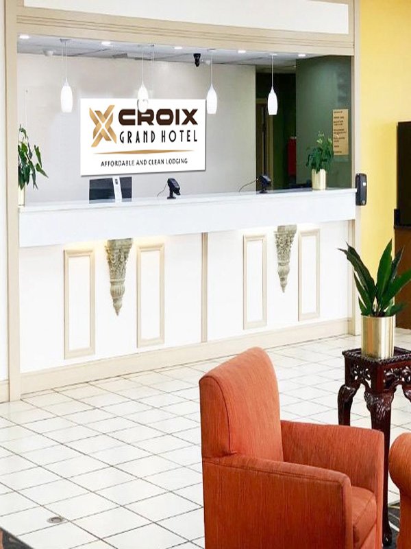 Hotel reception desk in Croix Grand Hotel with a sign, potted plants, and seating area.