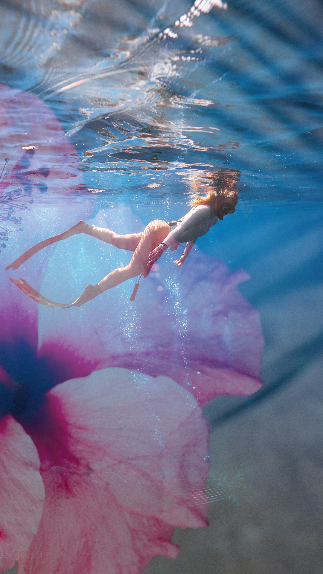 A woman swimming underwater with a pink flower overlay.