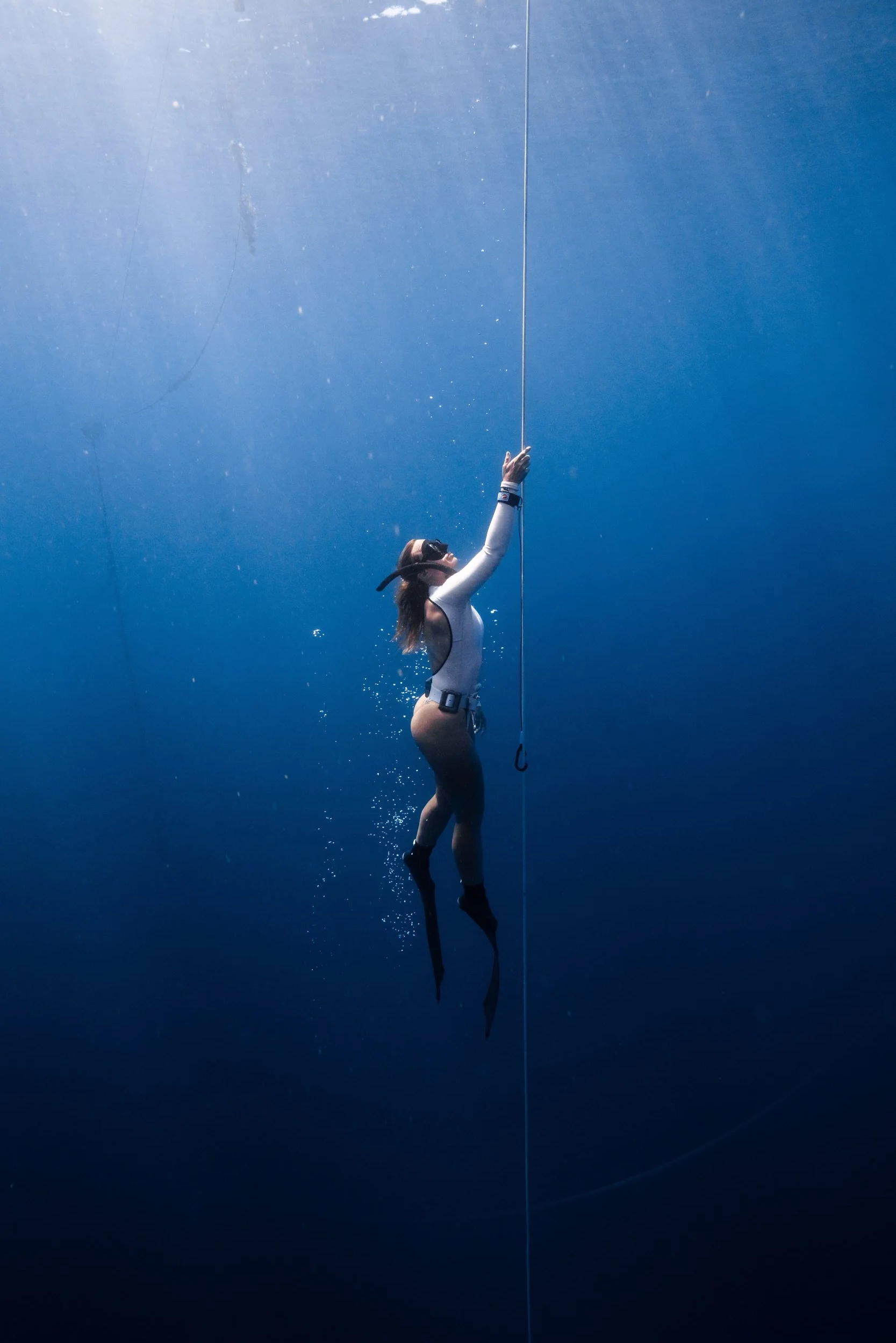 Woman in scuba diving gear reaching for a rope underwater.