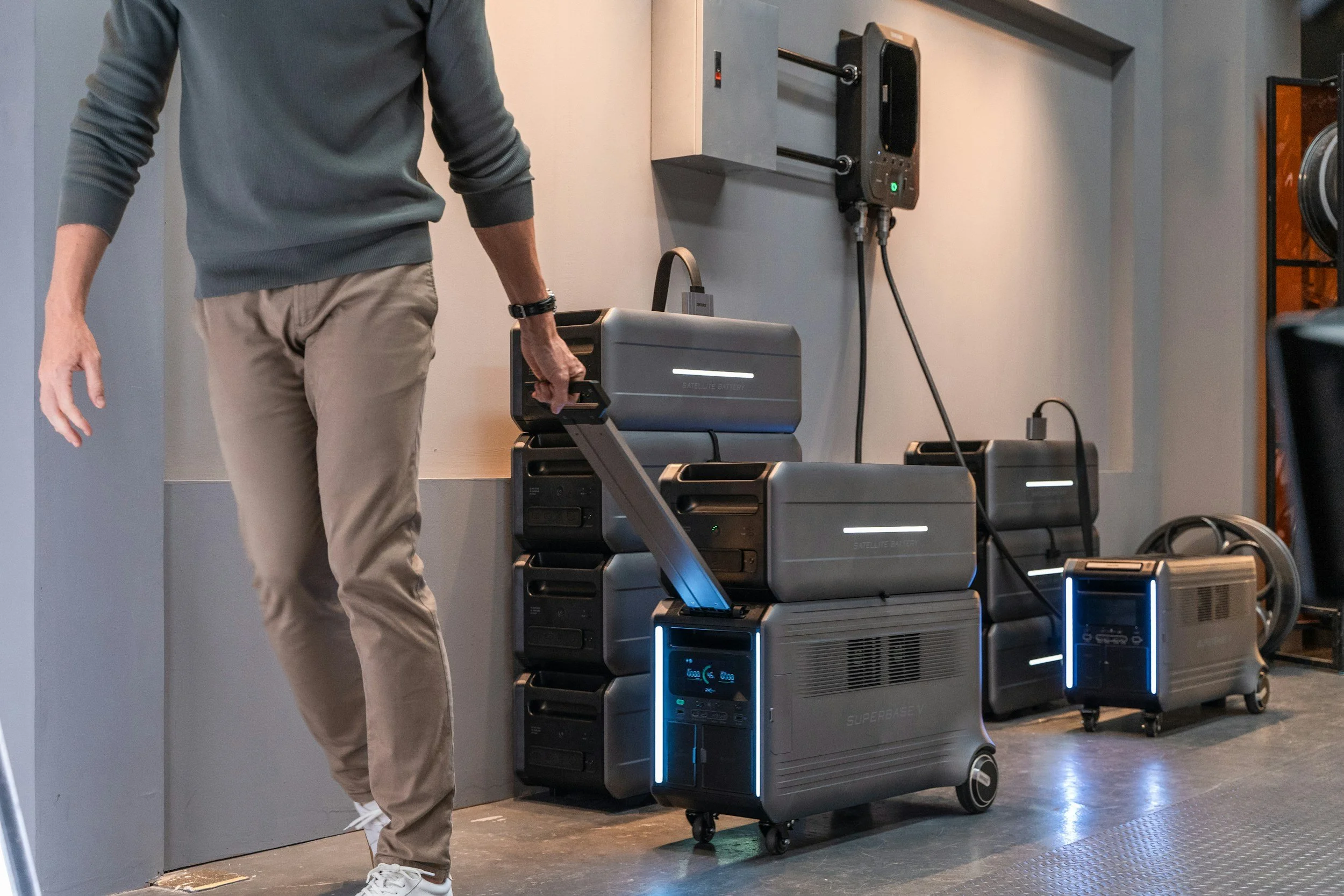 Man holding a portable satellite battery in a room with multiple energy storage batteries and electronic equipment.