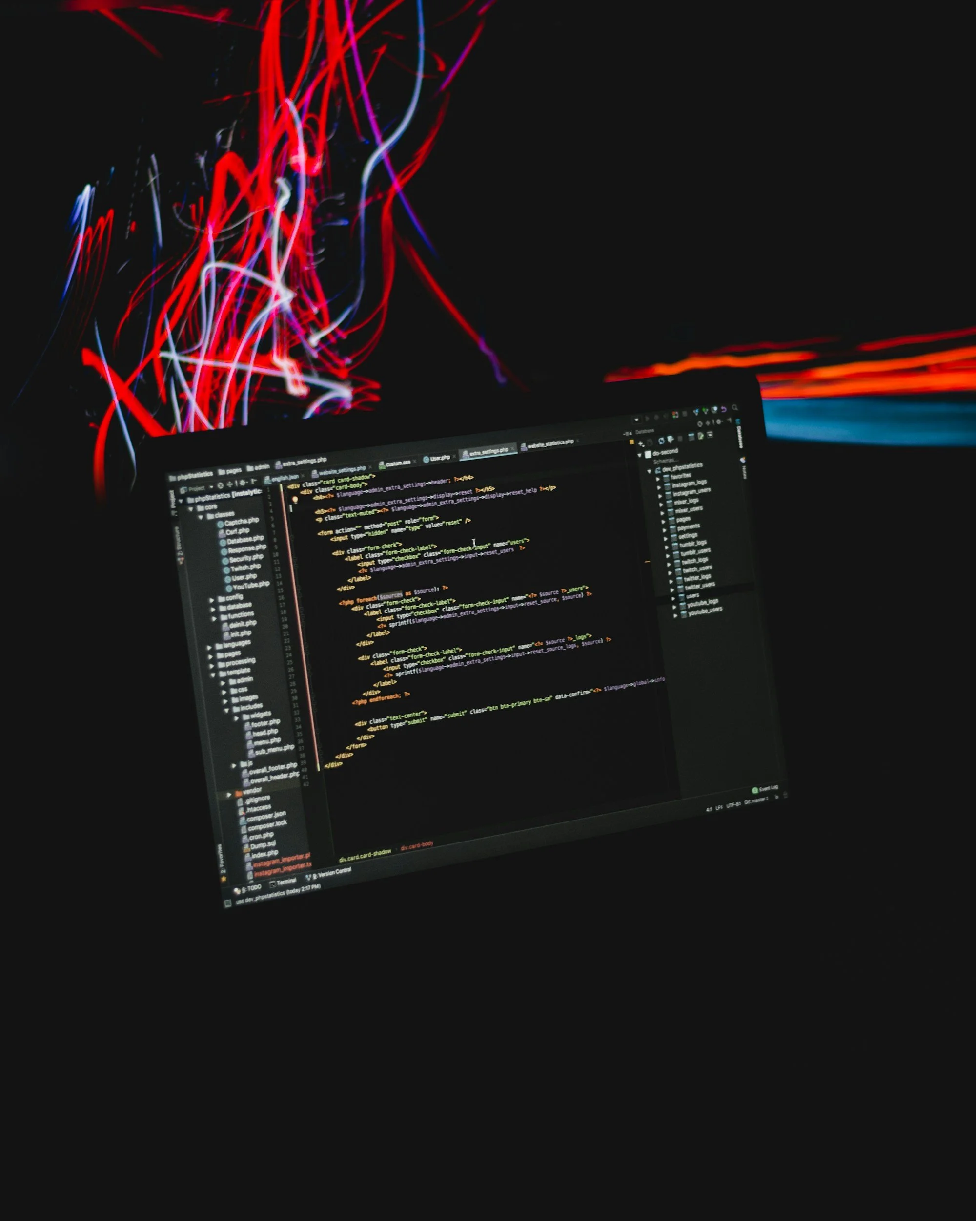 A computer screen displaying lines of code in a dark-themed code editor, with colorful abstract light streaks in the background.