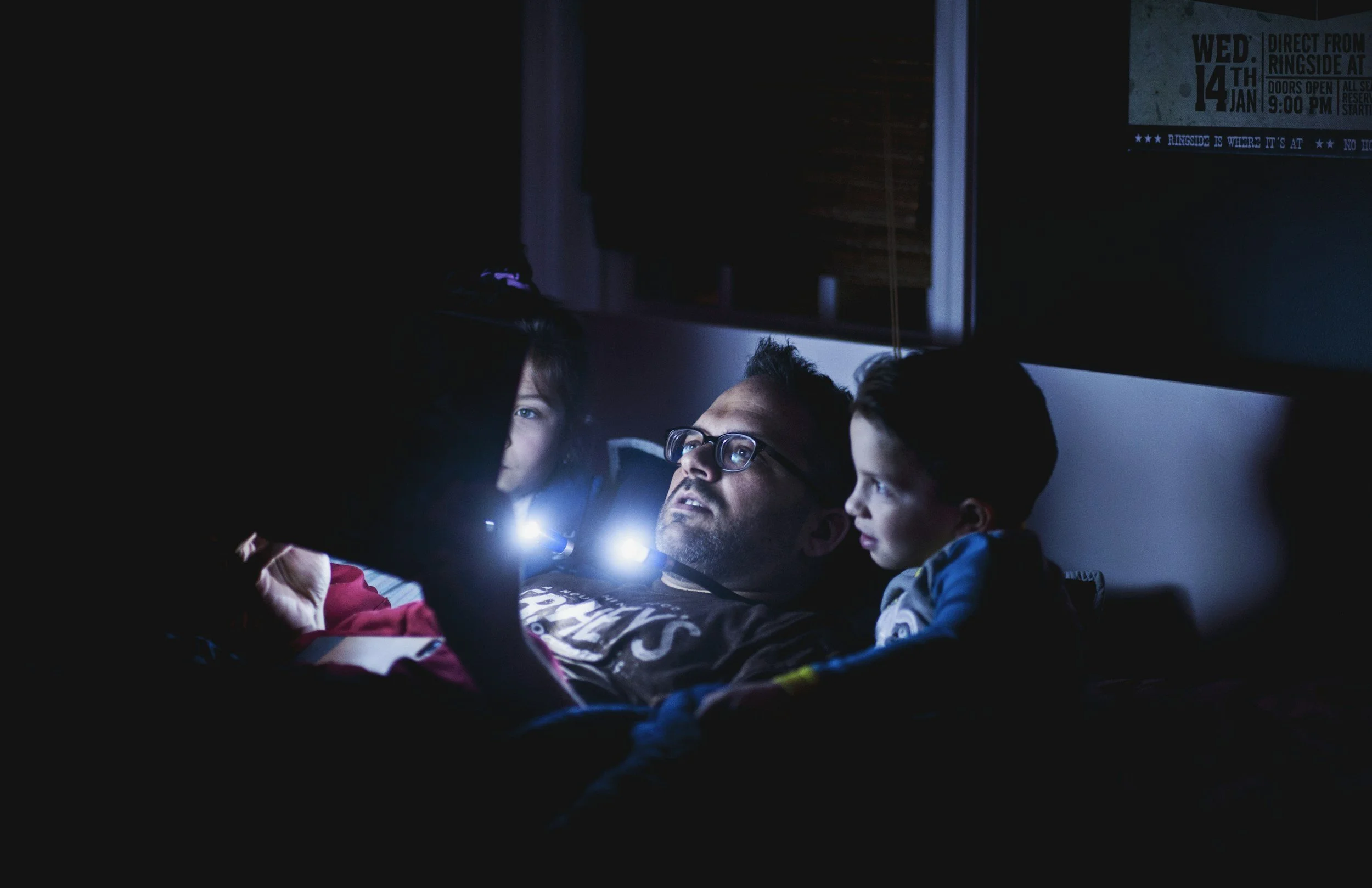 Three children and an adult closely examining something with a flashlight in a dark room.