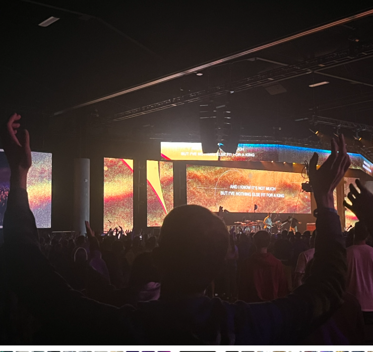 Crowd at concert with hands raised, large LED screens displaying colorful visuals and lyrics.