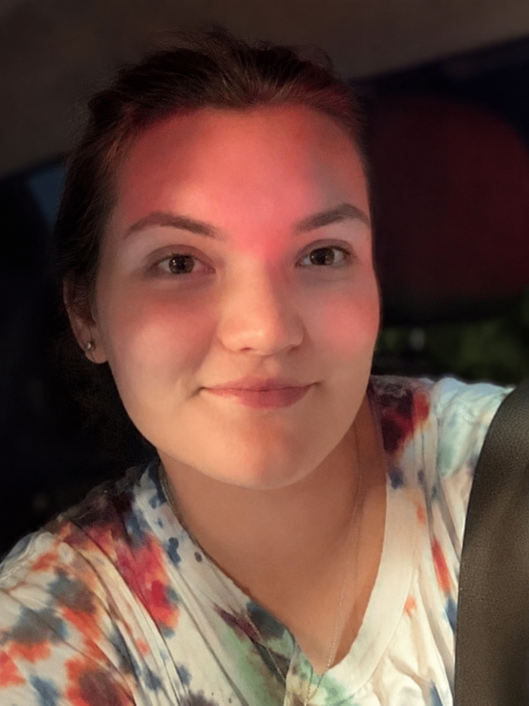 A young woman with short dark hair and earrings, smiling for a selfie inside a vehicle.