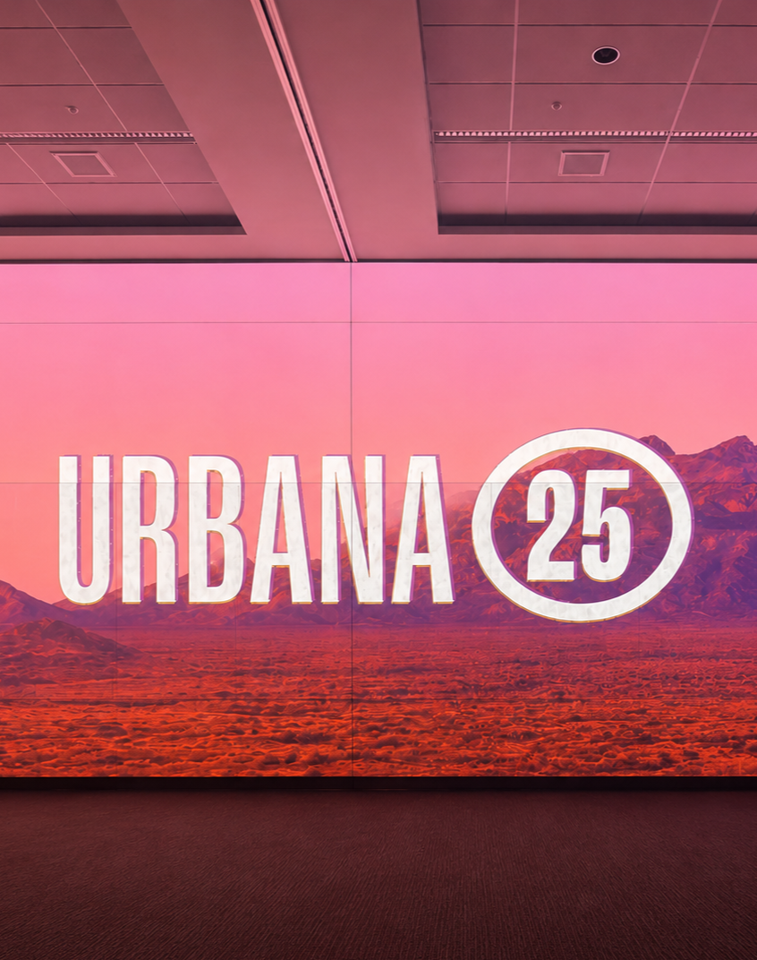 Bright pink display with the text 'URBANA 25' and a desert landscape background, mounted on a wall indoors.