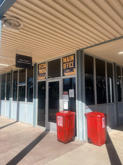 The exterior of a government building with signs indicating the main office, an official municipal department, and a welcome message. There are two red donation bins outside, and a digital display screen on the façade.
