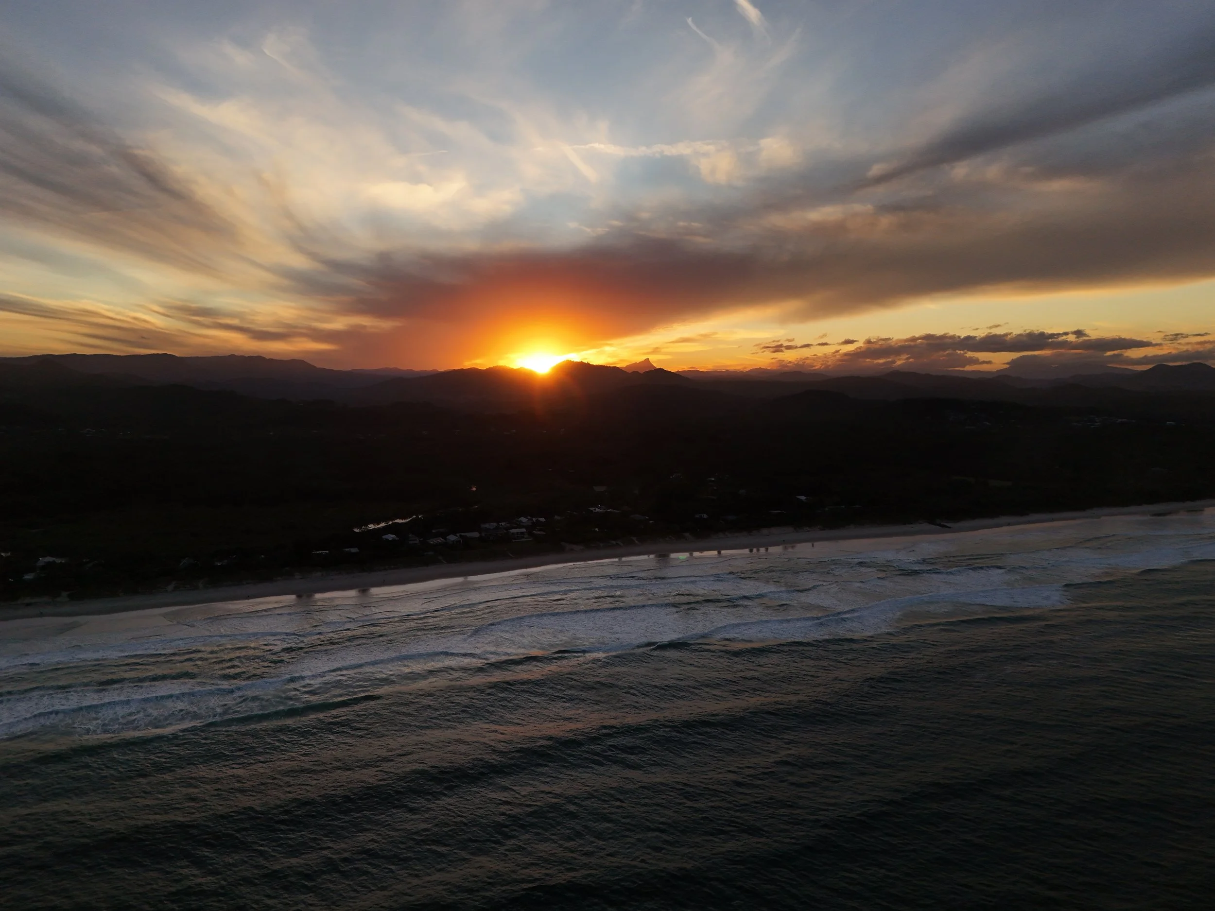 Sunset over the ocean with mountains silhouetted in the distance.