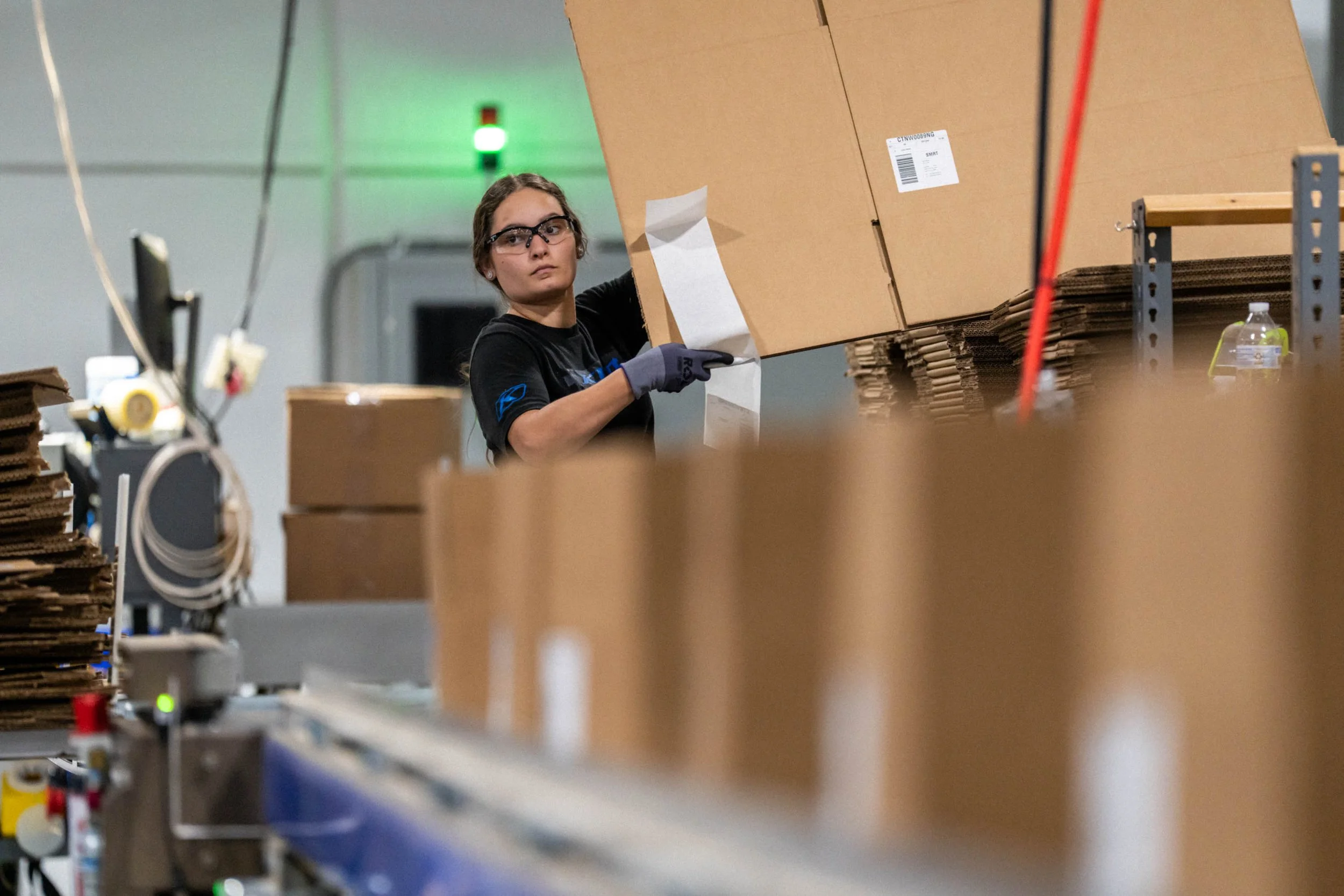 Worker handling cardboard boxes in what appears to be a warehouse or packaging facility.
