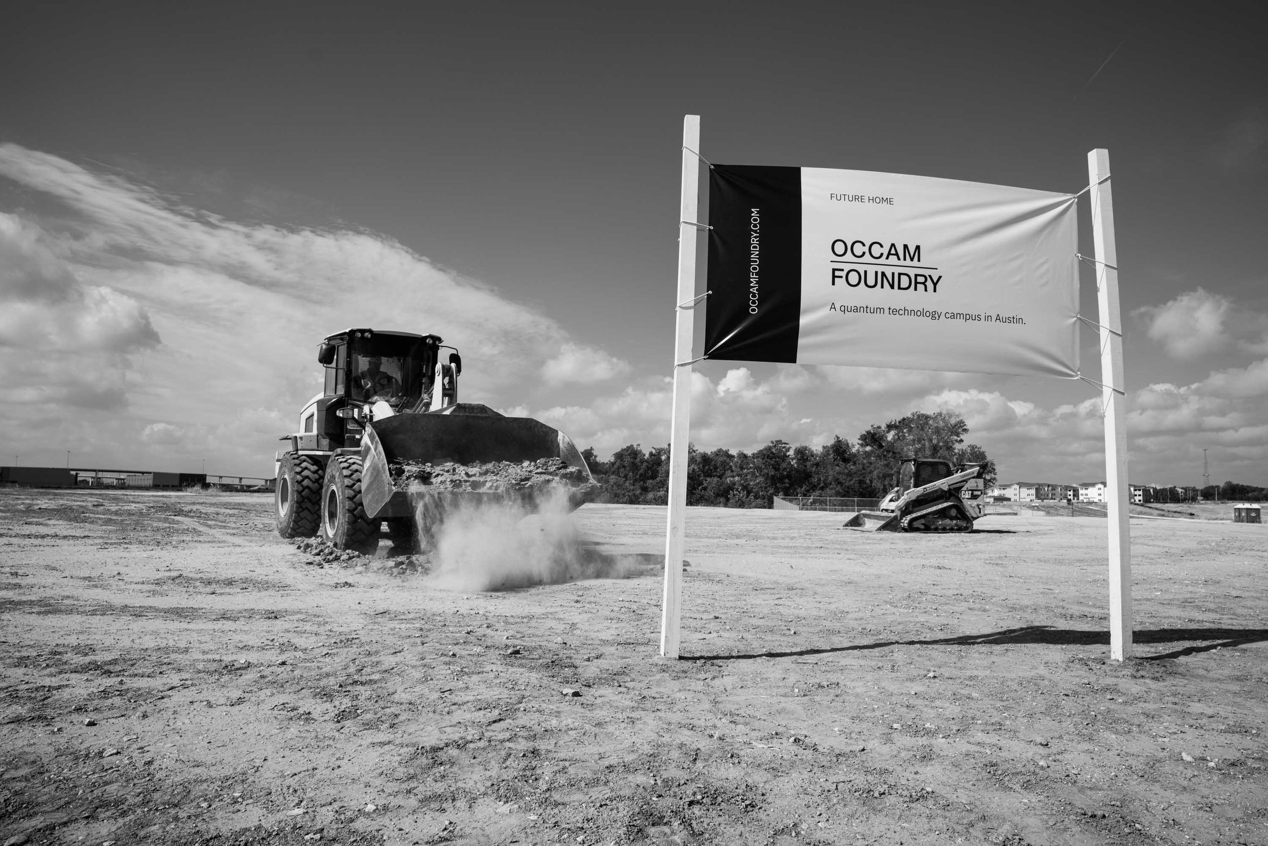 Construction site with a bulldozer moving dirt and a sign reading OCCAM FOUNDRY, indicating a future home for a quantum technology campus in Austin. The sky is partly cloudy.